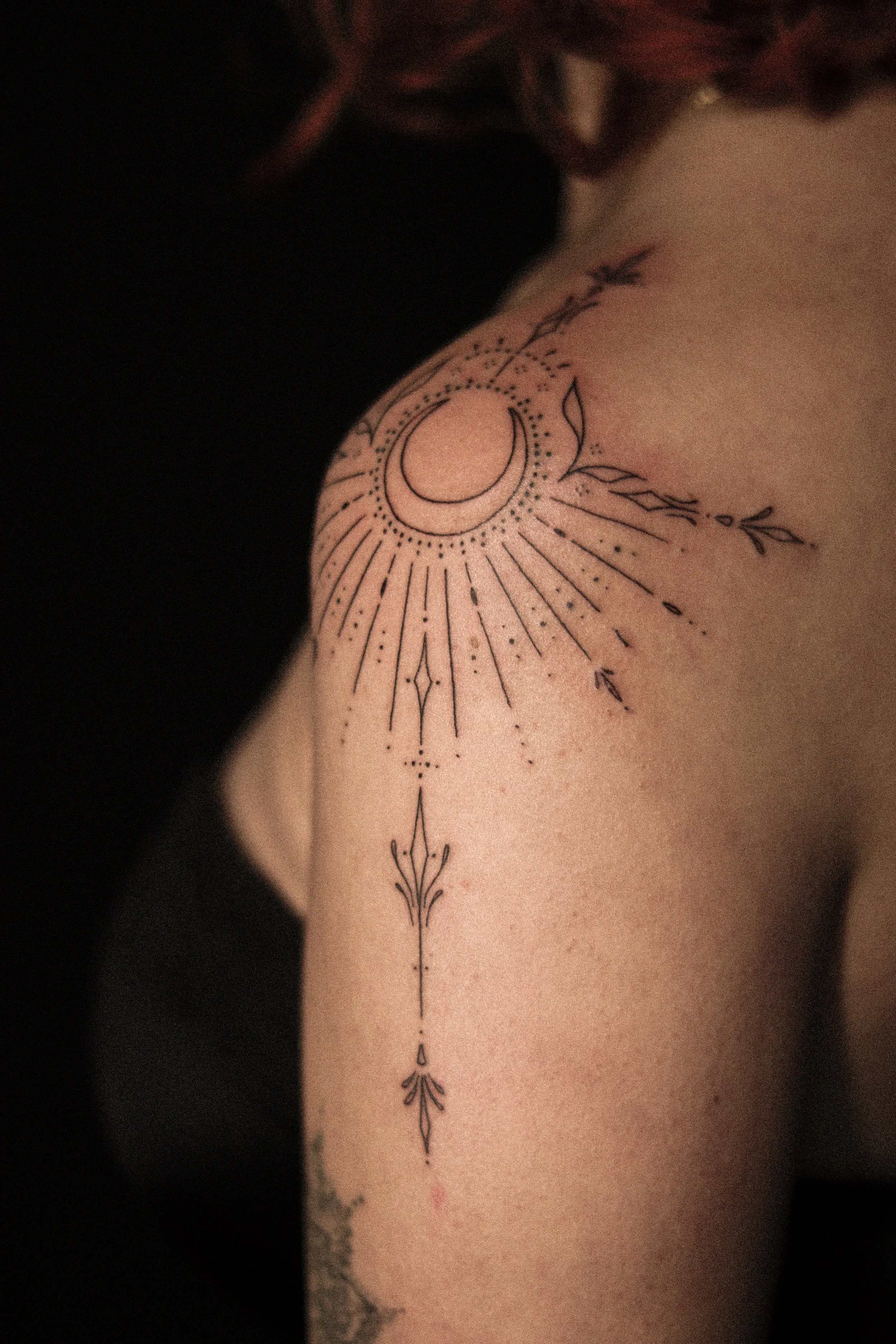 Tatoeage van een maan, stralen en lijnen op de schouder en bovenarm.