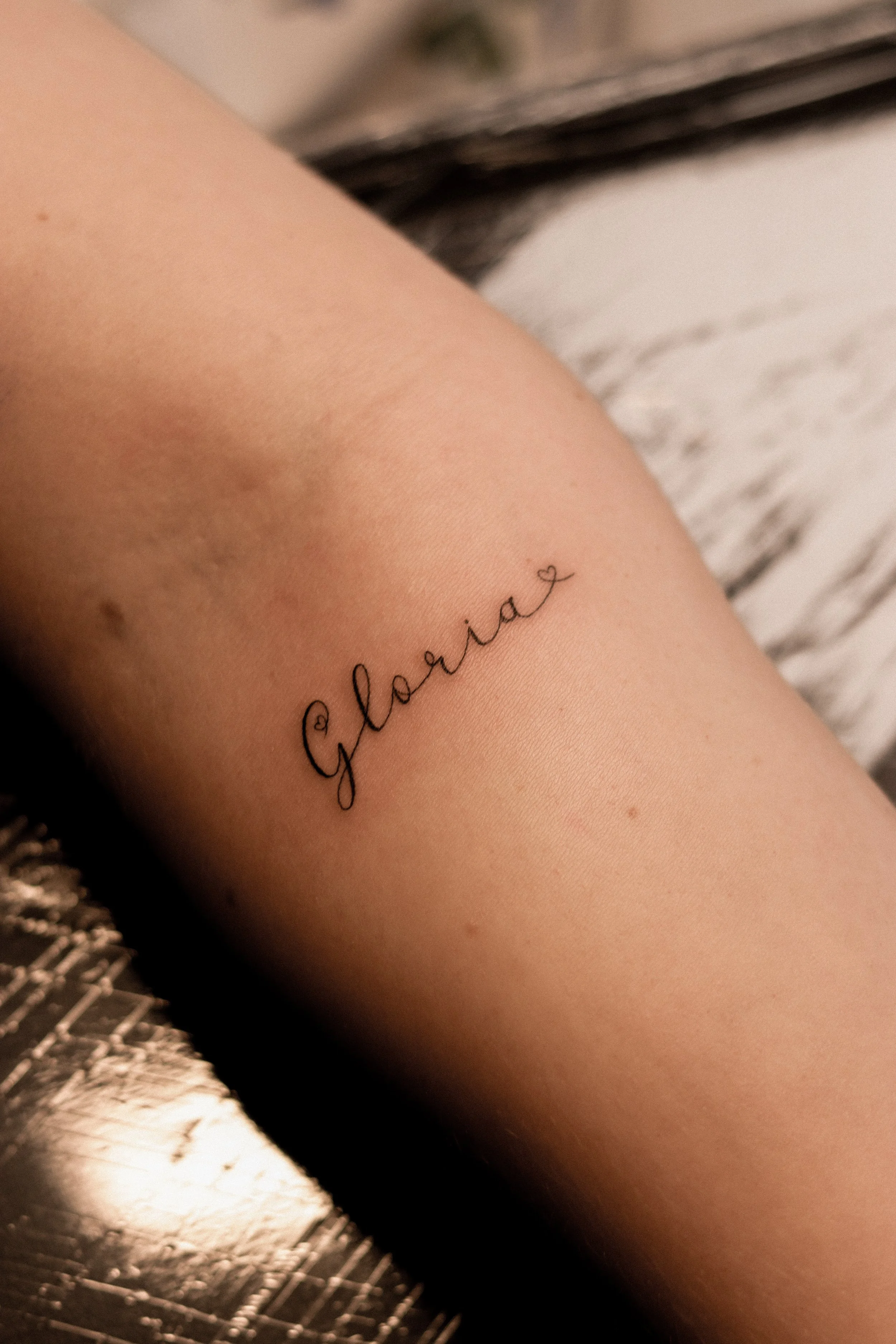 Tattoo met de naam 'Glaria' en een klein hartje op een mensenarm.