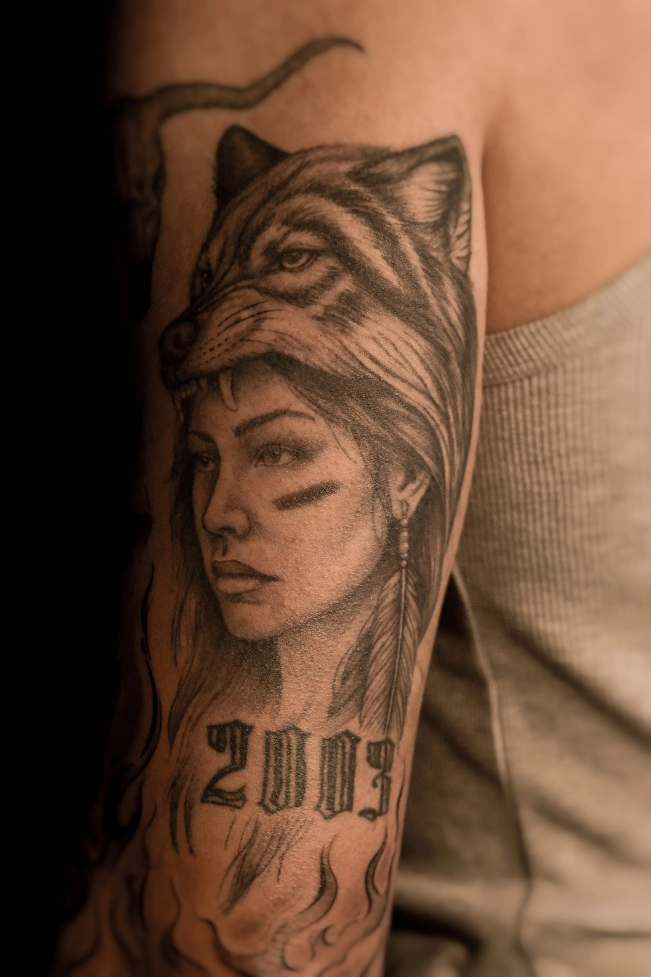 Een tatoeage op de bovenarm van een vrouw met veren en een wolf, met de tekst 'WILD' onderaan.