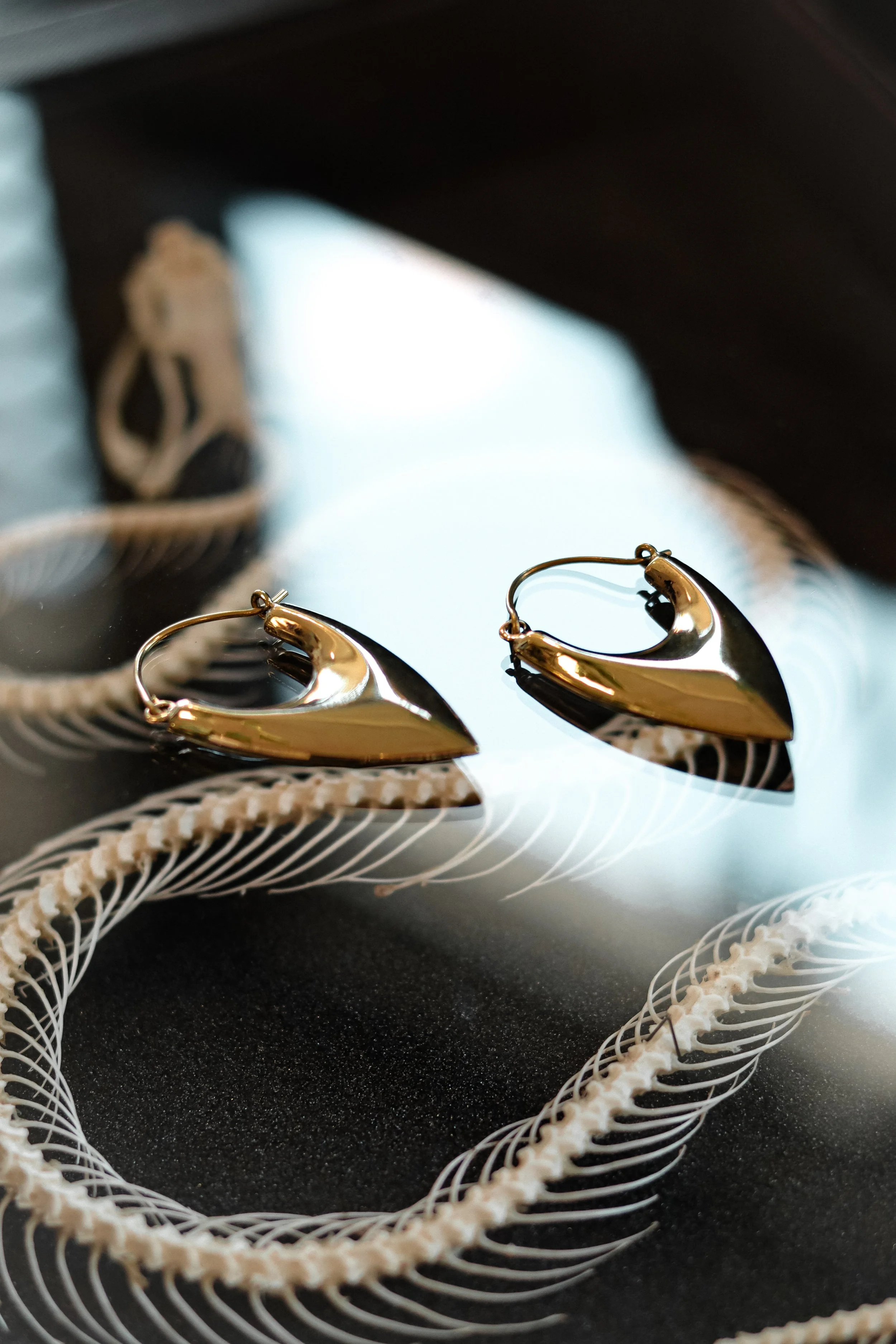 Gouden oorbellen liggen op een reflecterende zwarte ondergrond met witte sieraden rondom.