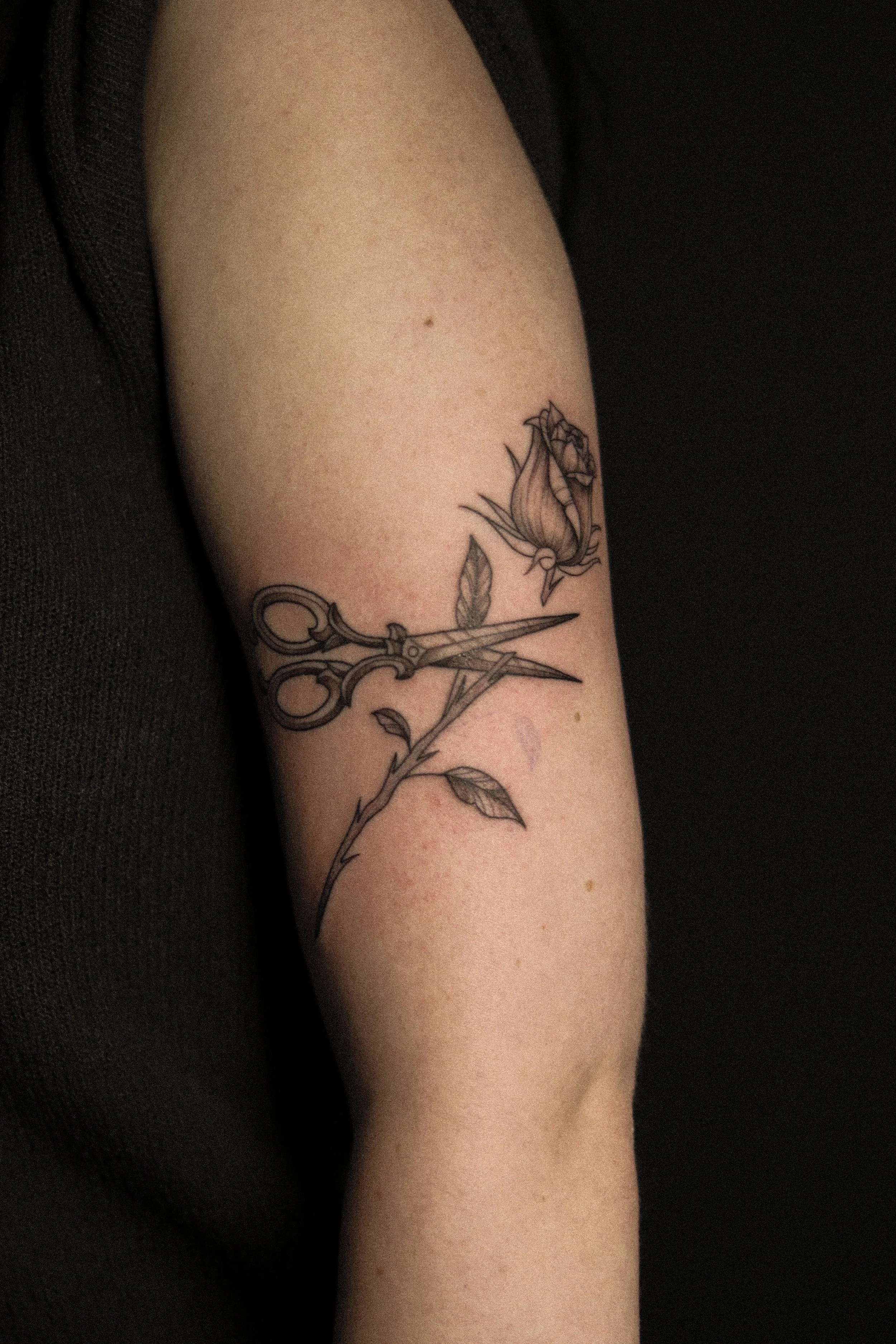 Tattoo van een roos, een schaar en een naald op de bovenarm.