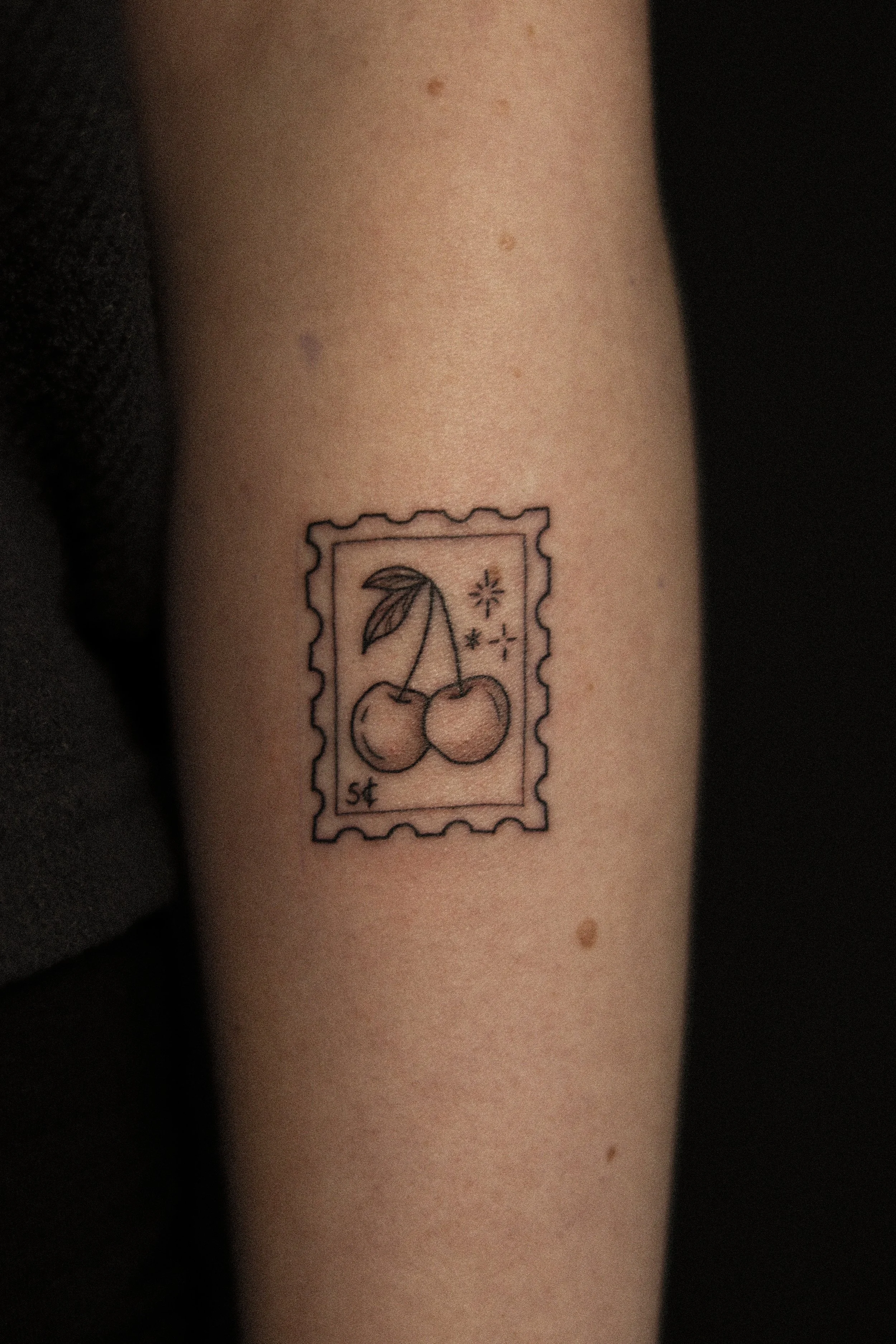 Tatoeage van een postzegel met een tekening van twee kersen, enkele sterren en een stip.