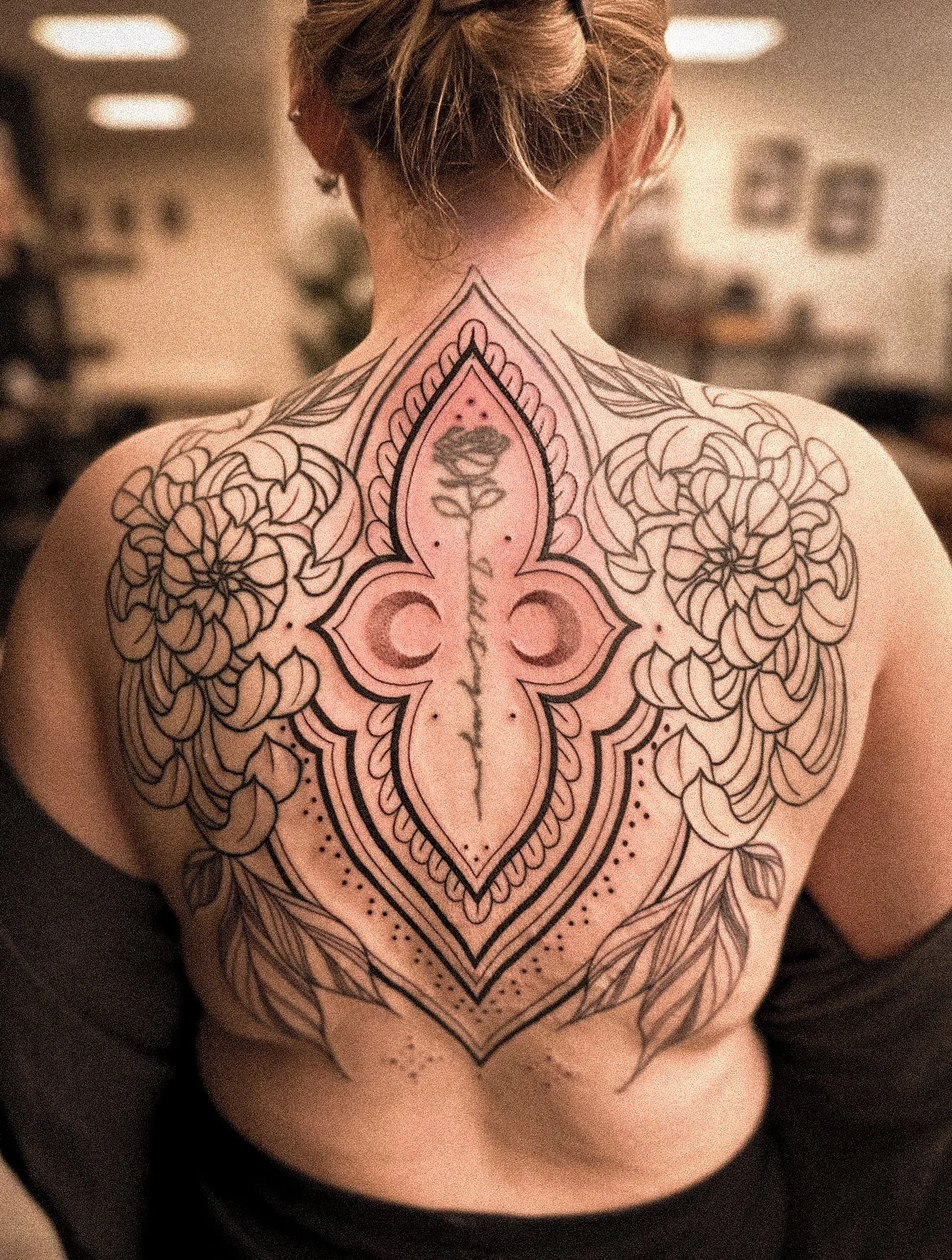 Een persoon met een grote rugtattoo met bloemmotieven en een middenlijn met de tekst 'In love with my own style'.