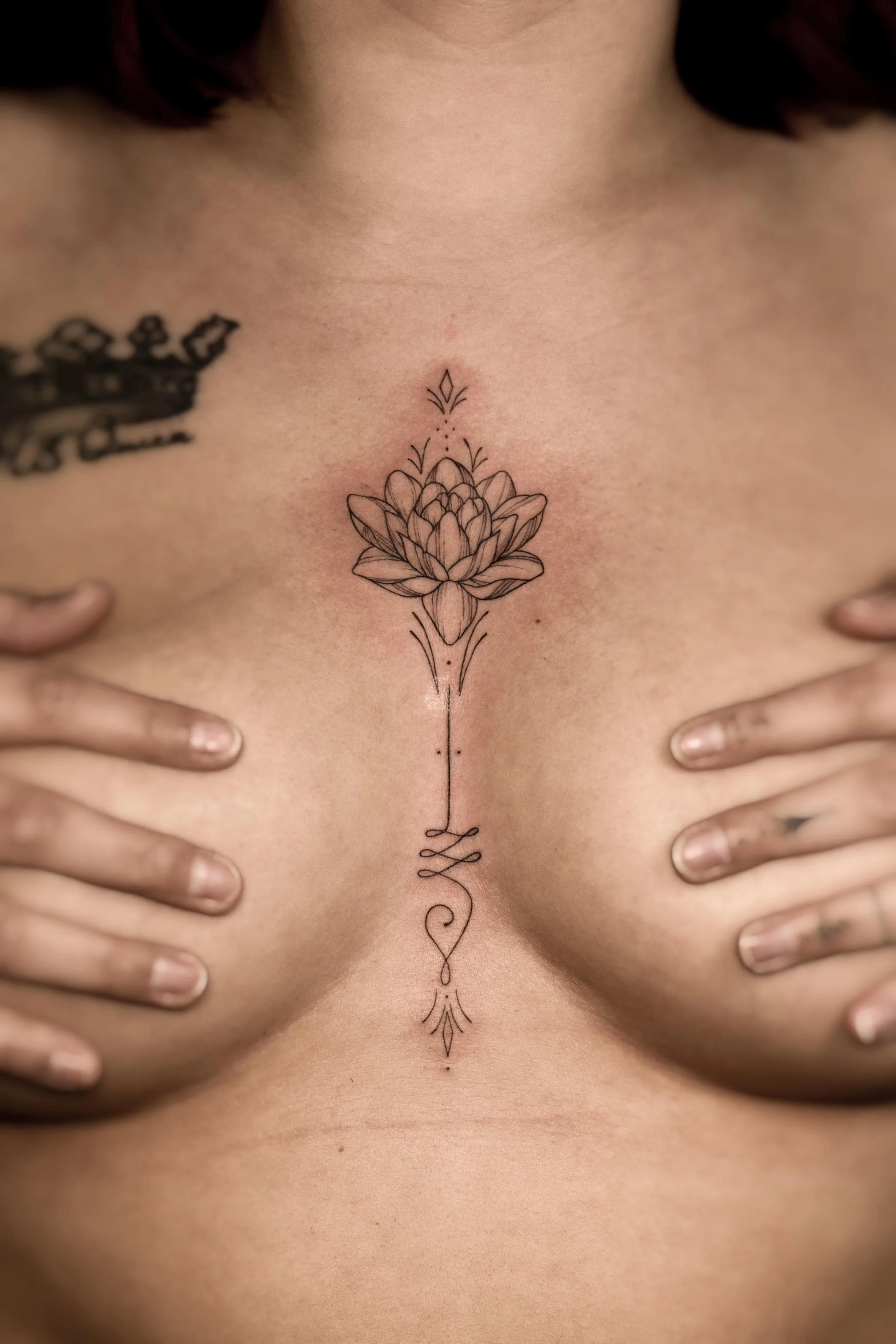 Tattoo van een gestileerde bloem op de borst met hand erbij.