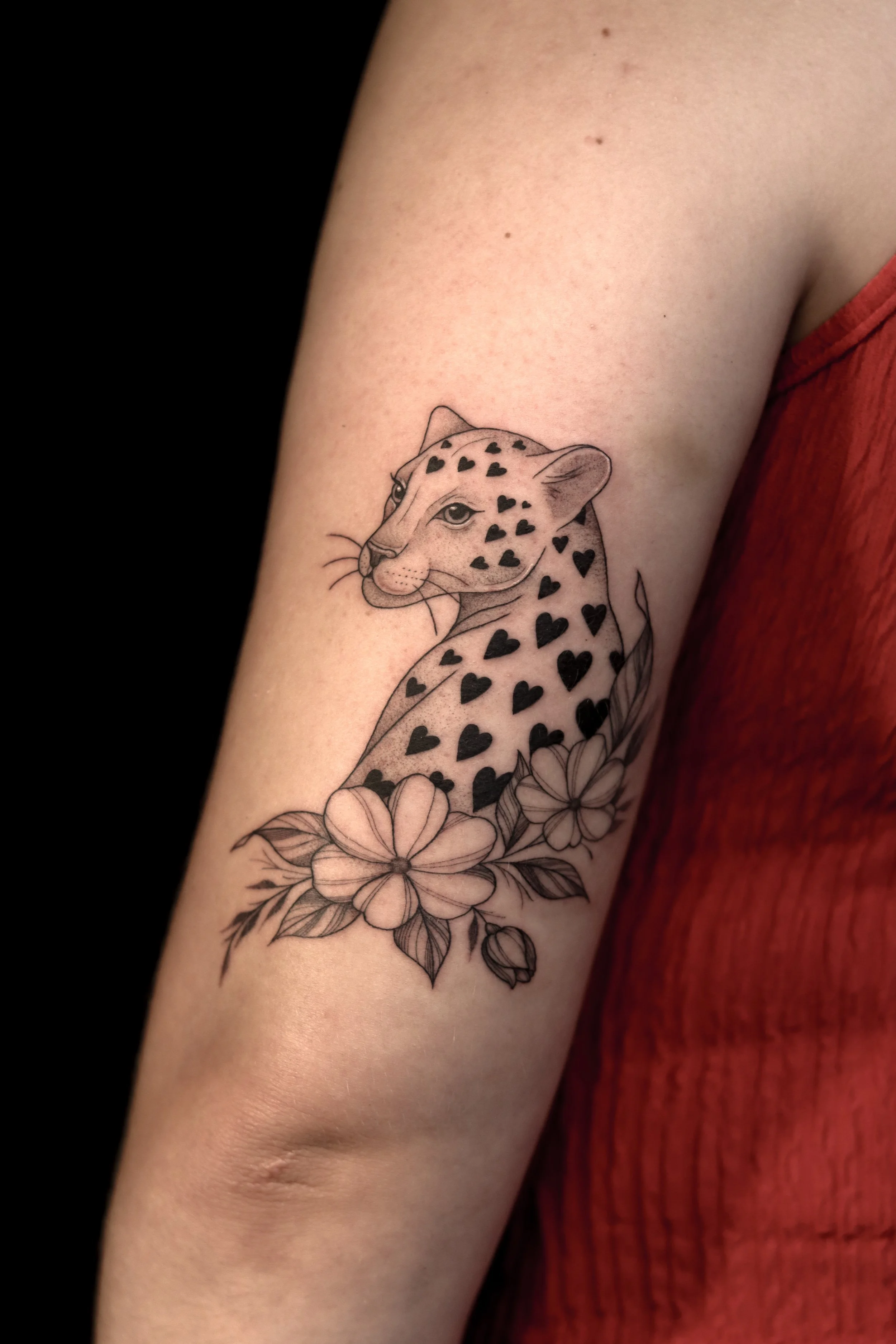 Tatoeage van een jaguar met hartpatronen en bloemen op de bovenarm.