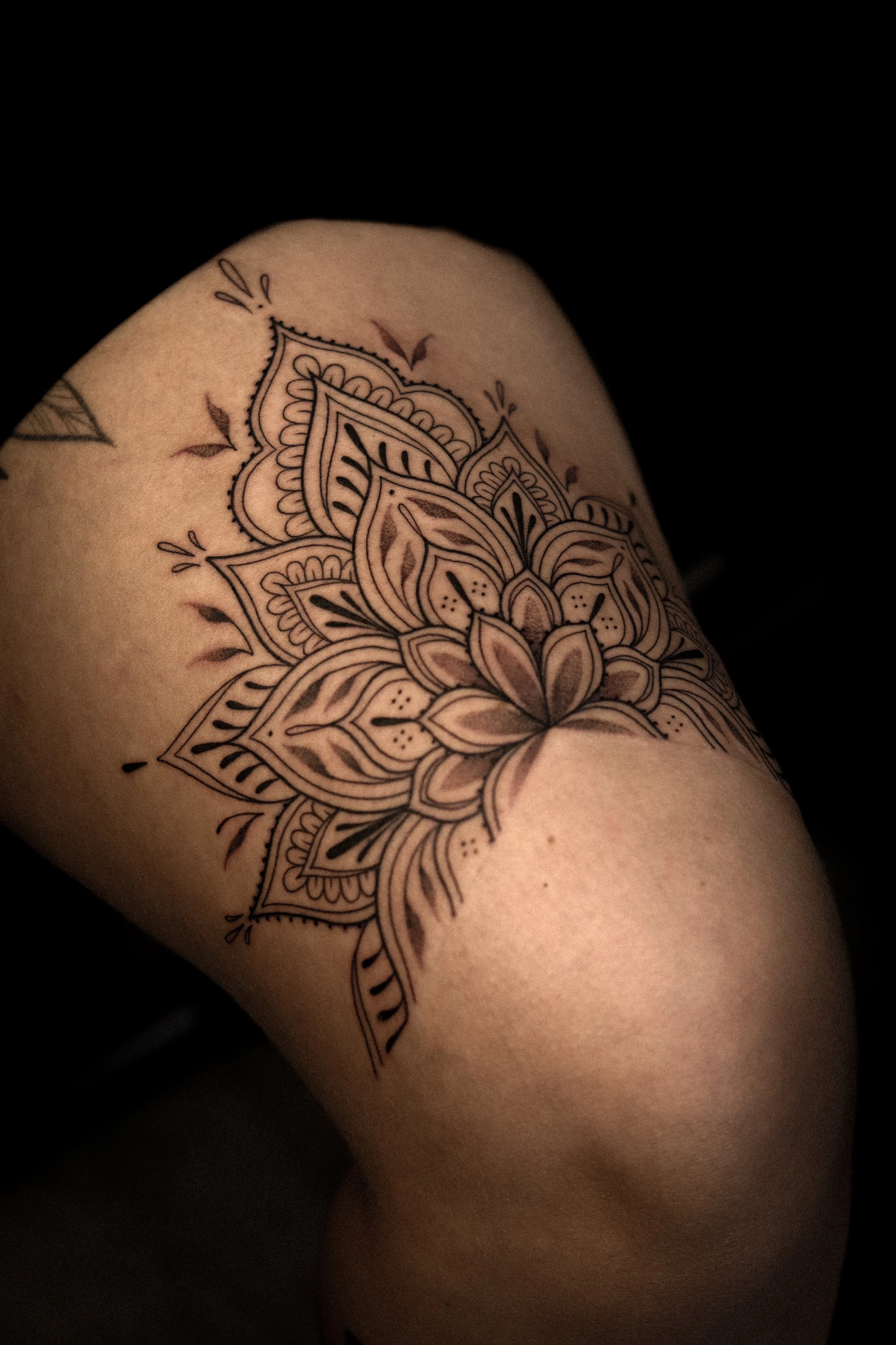 Tattoo van een mandala op de dij, met bloemmotieven en details in zwart en grijs