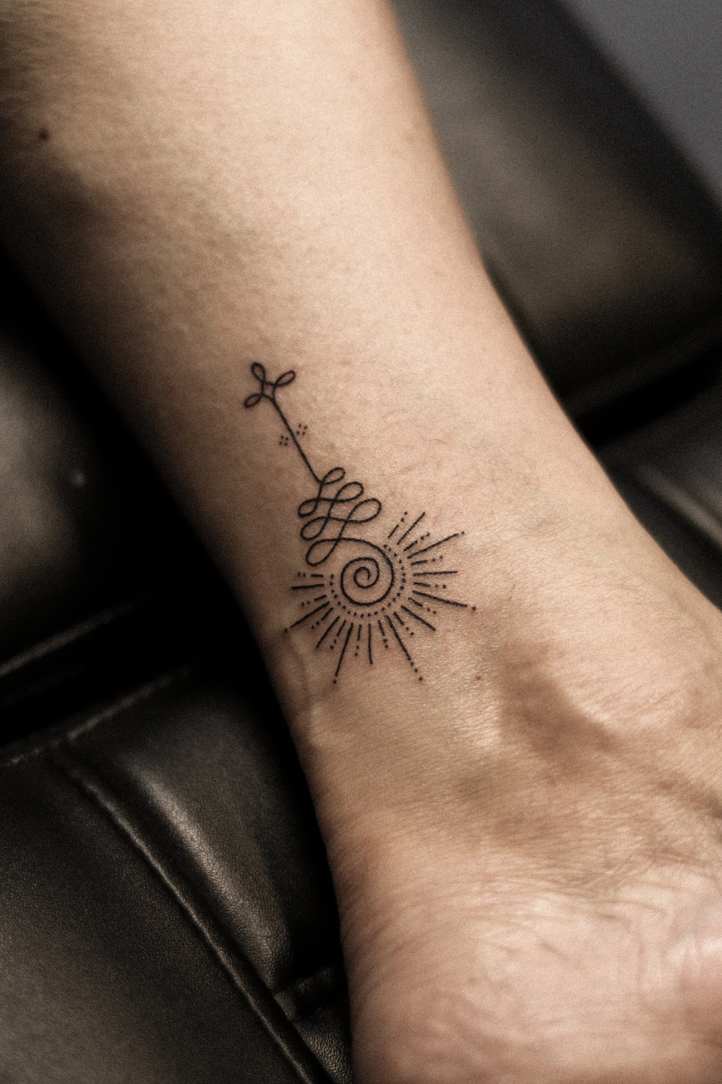 Tatoeage op pols met een sun en een spirale inkt. Mooi, minimalistisch design.