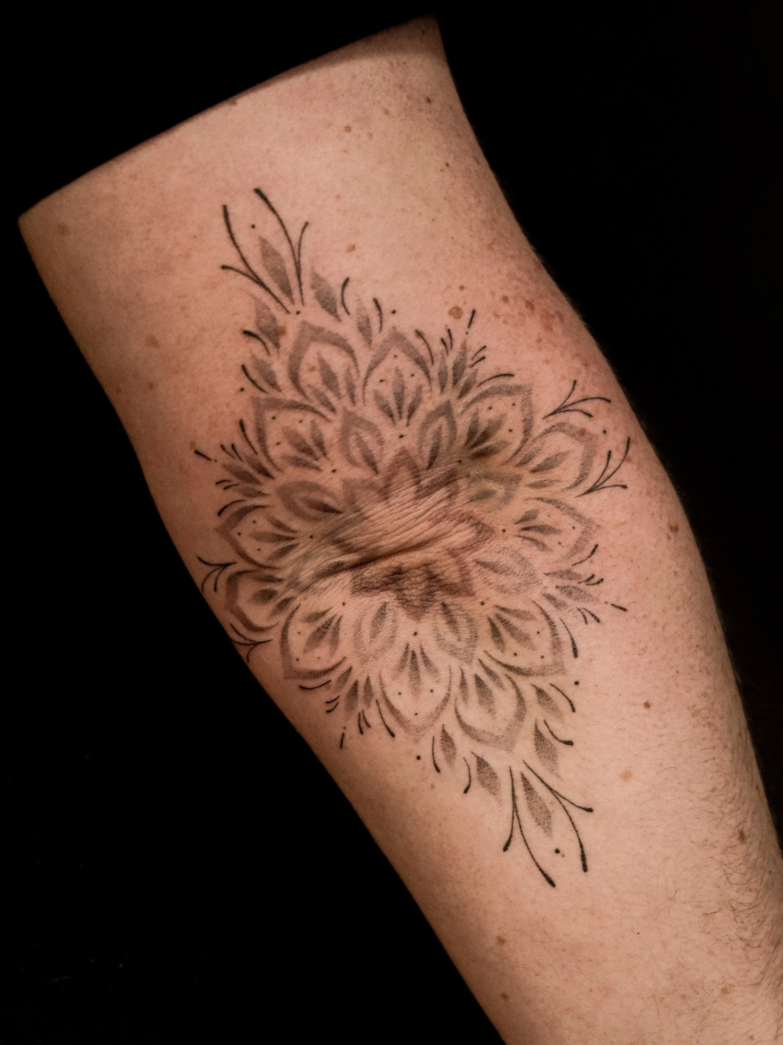 Tattoo van een bloem op de onderarm met zwarte inkt en gedetailleerde lijnen.