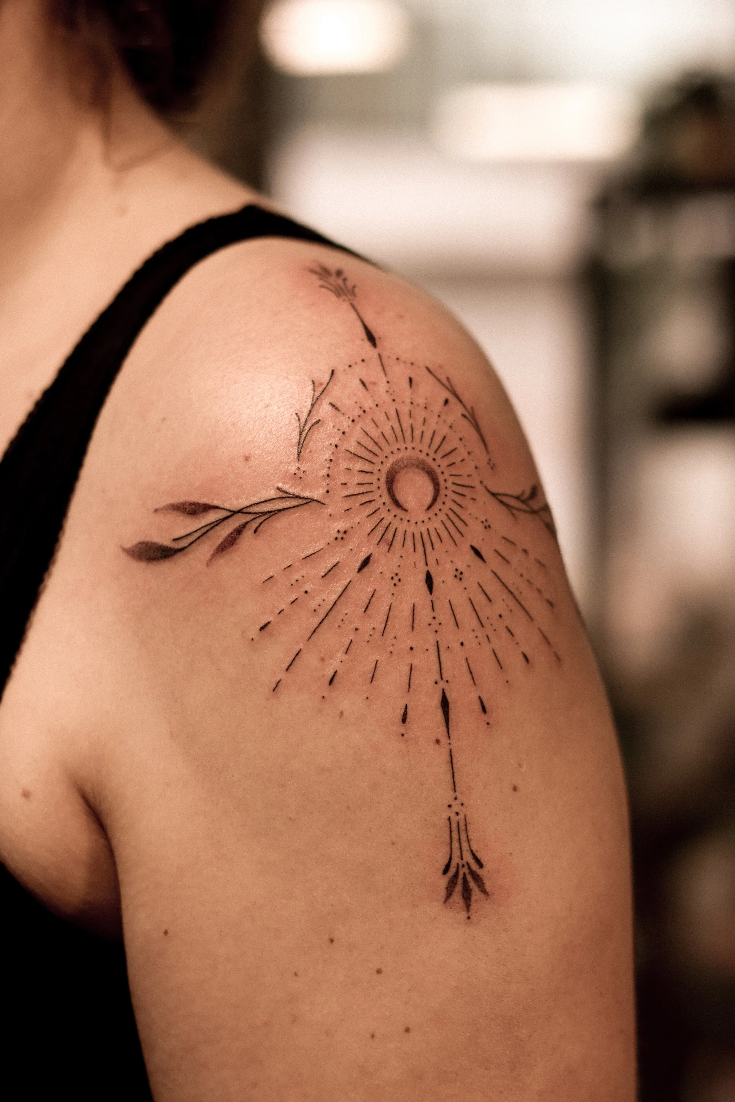 Tattoo op schouder met een abstracte zon en pijlen.