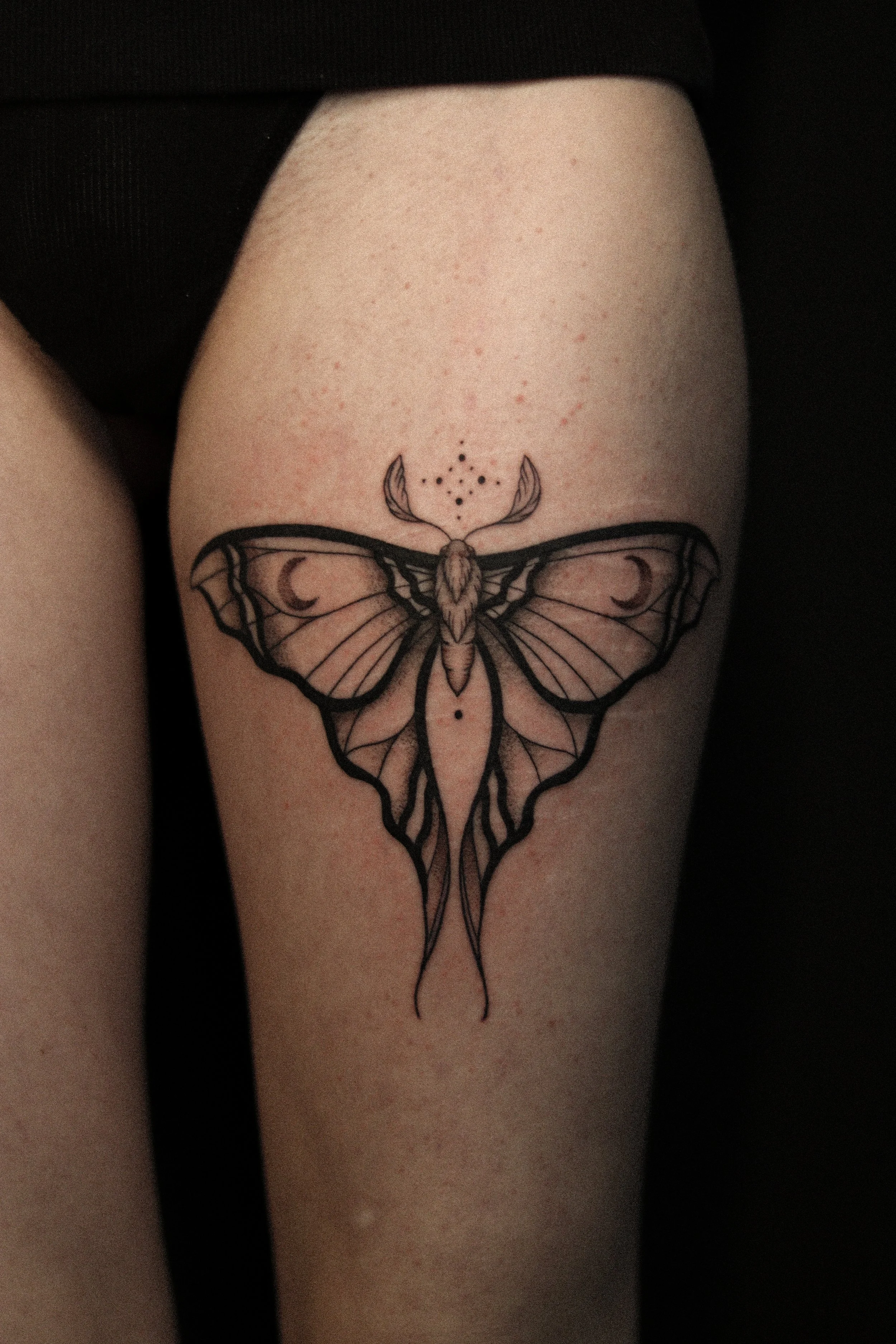 Tatoeage van een geometrische vlinder op een bovenbeen.