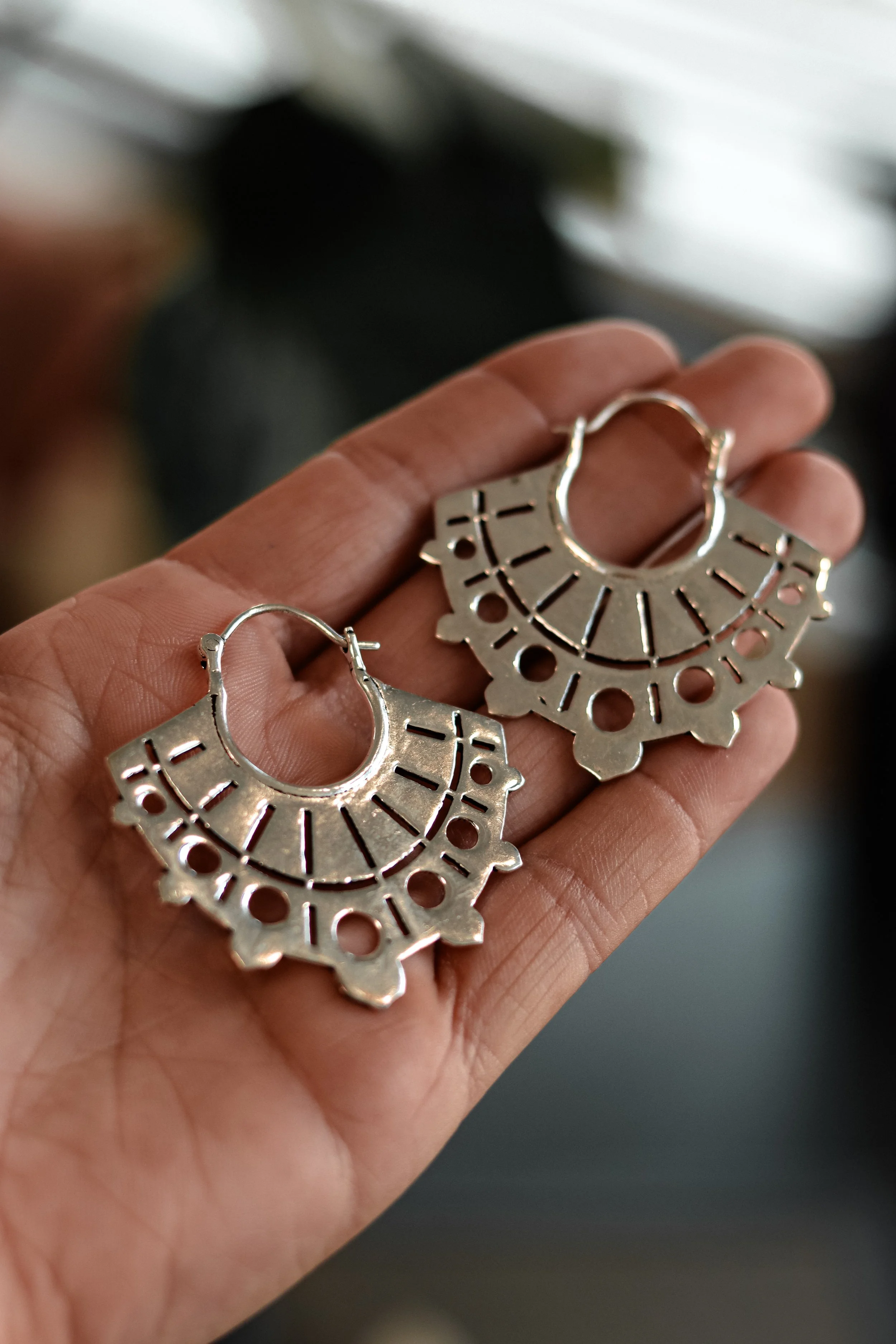 Persoon houdt een paar grote, zilveren, geometrische oorbellen met openingen en cirkelvormige patronen.