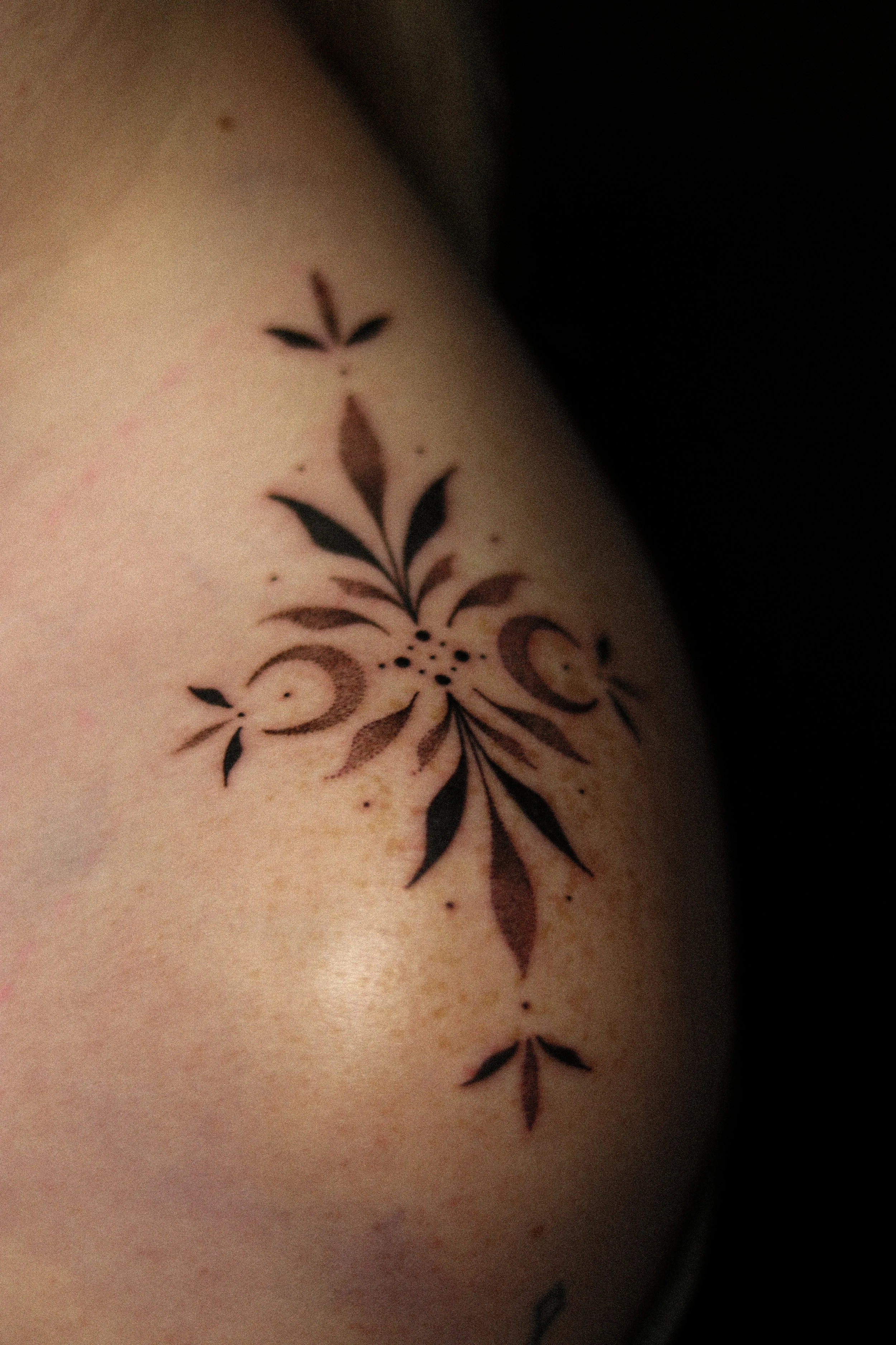 Een close-up van een tatoeage op de schouder met een bloemen- en bladmotief in zwarte inkt.