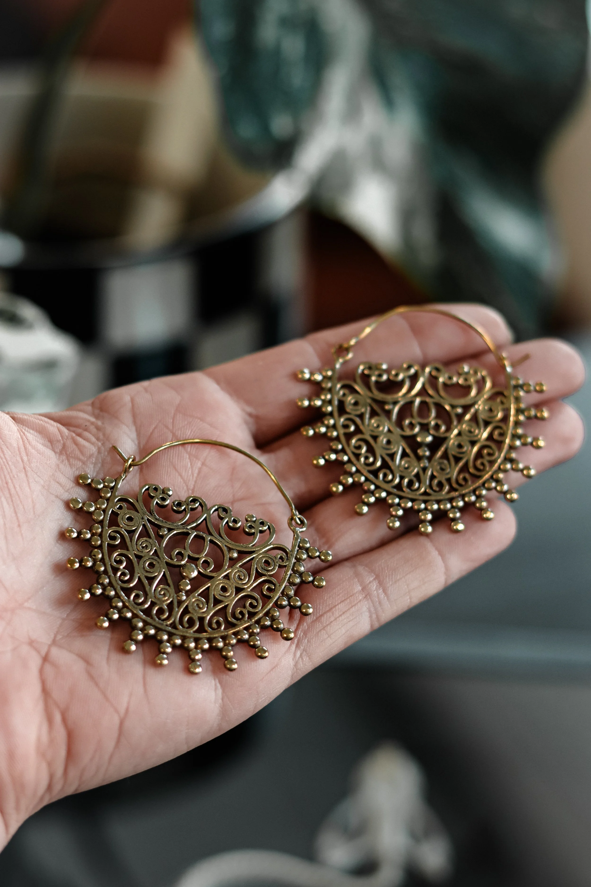 Goudkleurige gefantaseerde oorbellen met opengewerkte patronen en kleine rondjes, gehouden in een hand