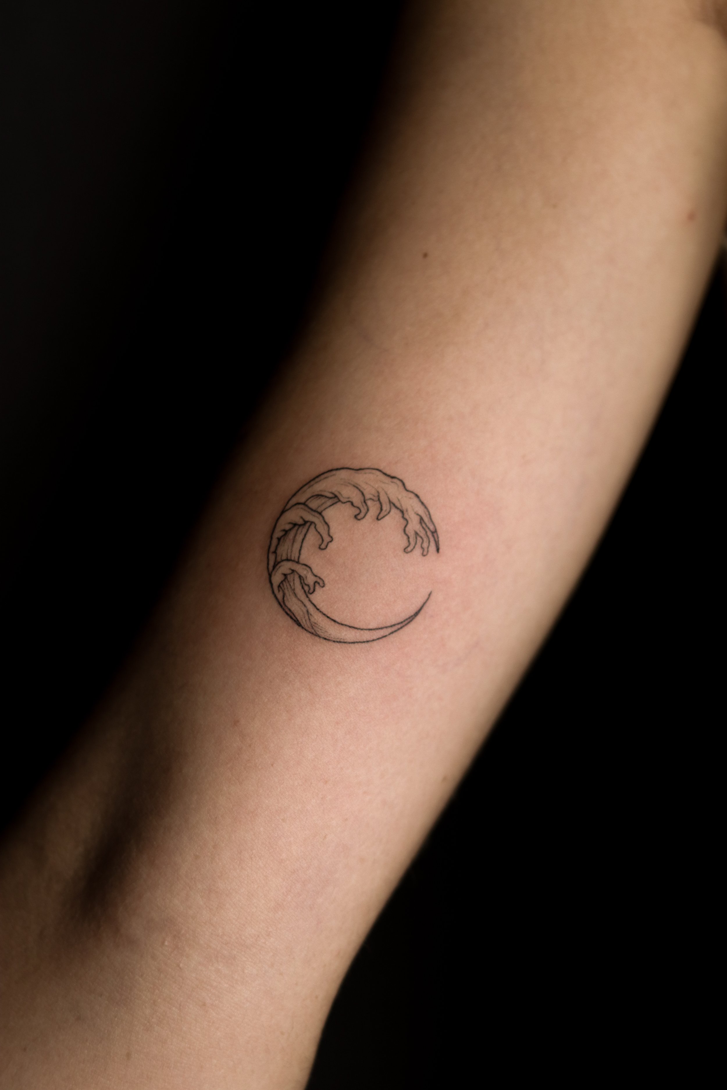 Een tattoo van een maan met golven op een onderarm