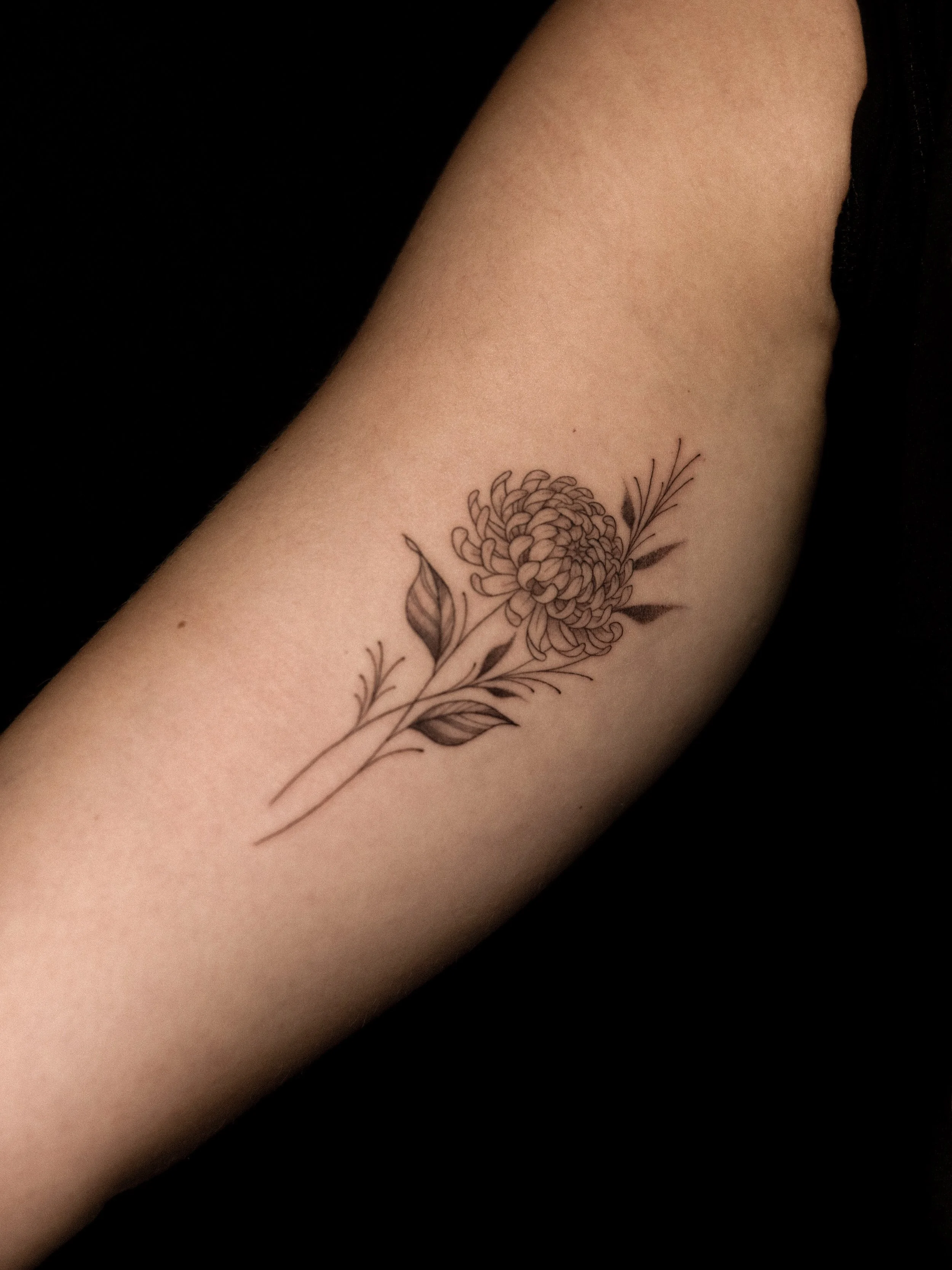 Tatoeage van een bloem met bladeren en stelen op de bovenarm.
