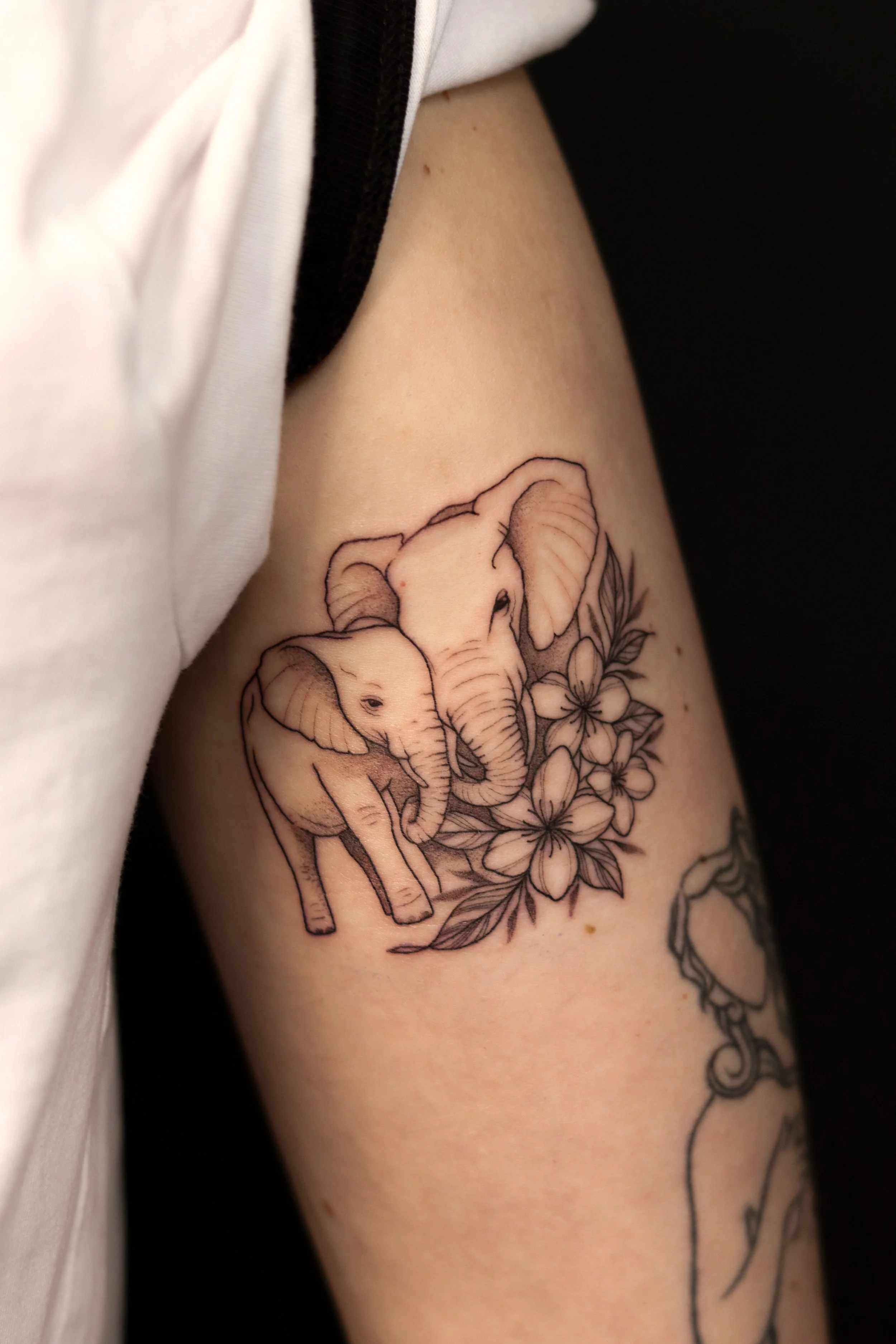 Tatoeage van twee olifanten en bloemen op een arm.