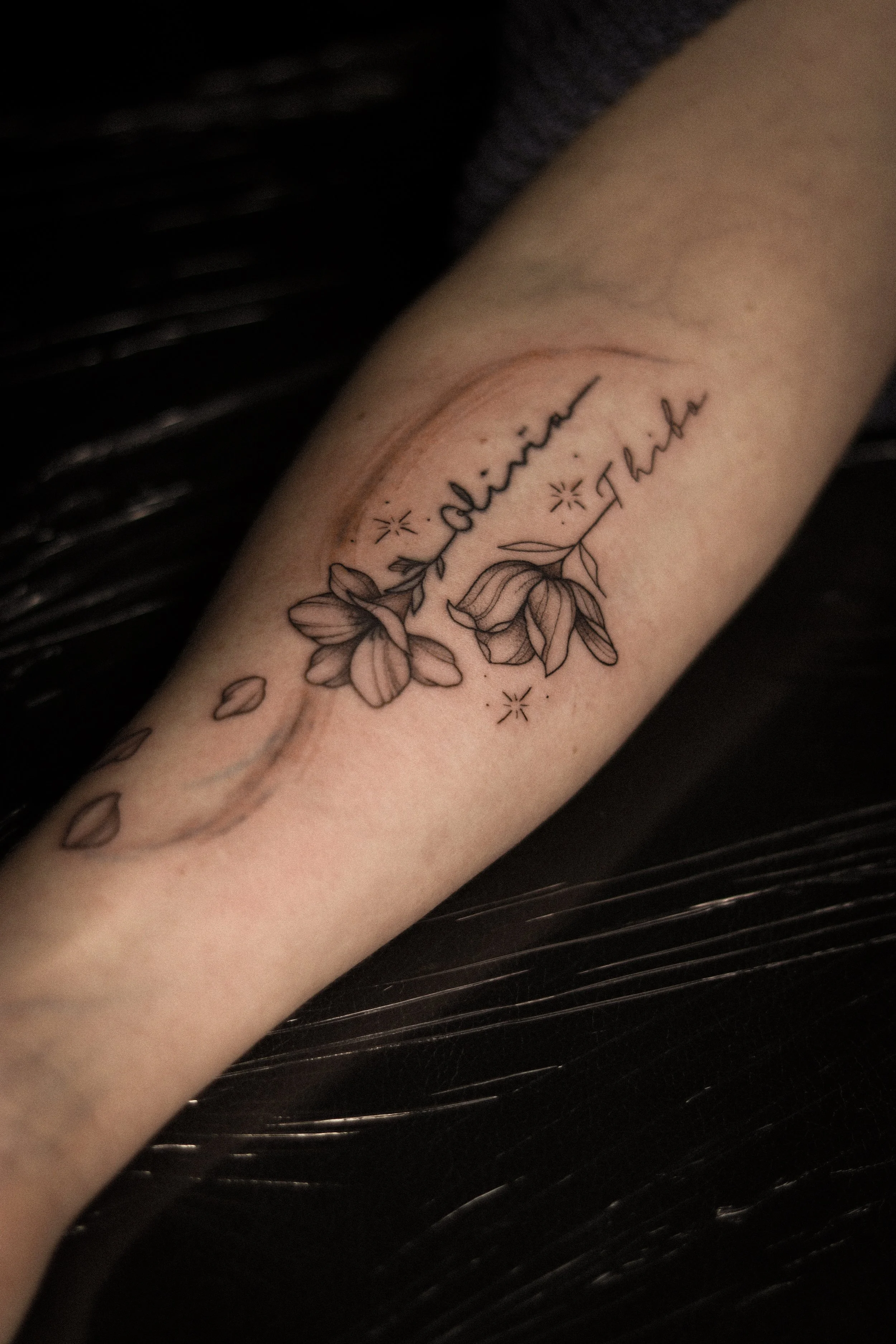 Tatoeage van bloemen en de woorden 'jaline' en 'Flor' op de onderarm.