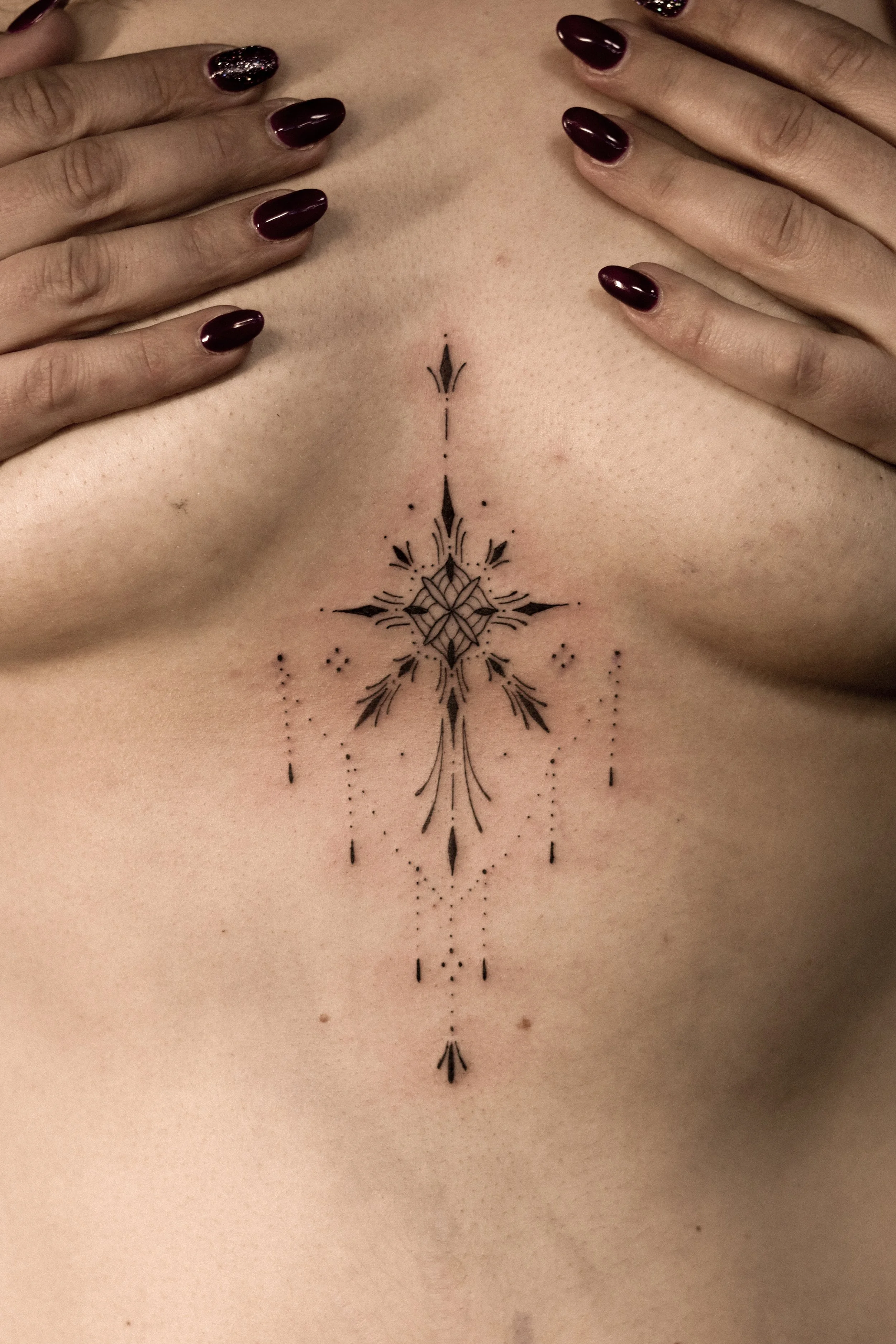 Een close-up van een tattoo op de buik, met een symmetrisch, decoratief ontwerp met lijnen en stippen.