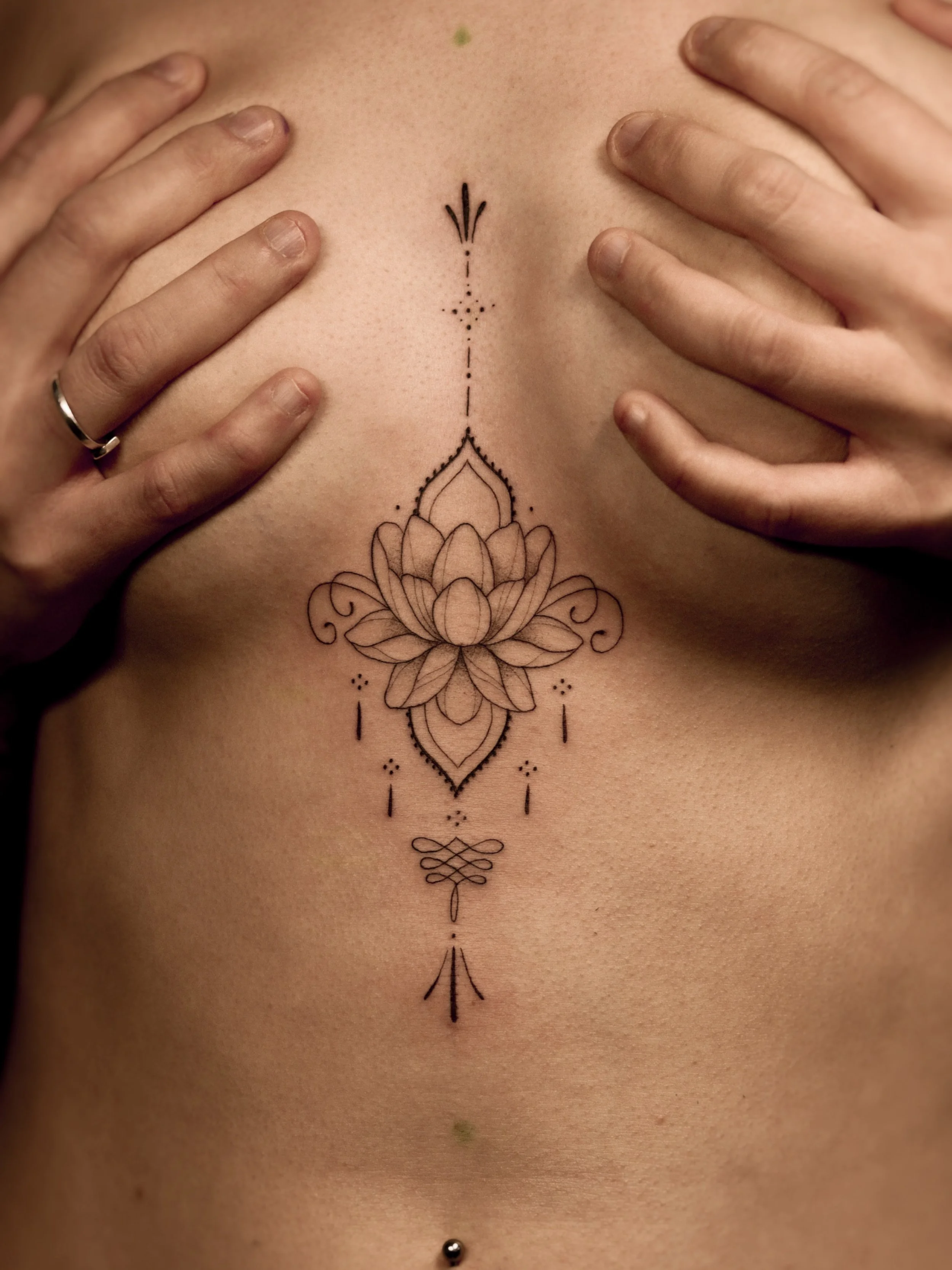 Een tattoo op het midden van de borst, met een lotus bloem en sierlijke lijnen en stippen eromheen.