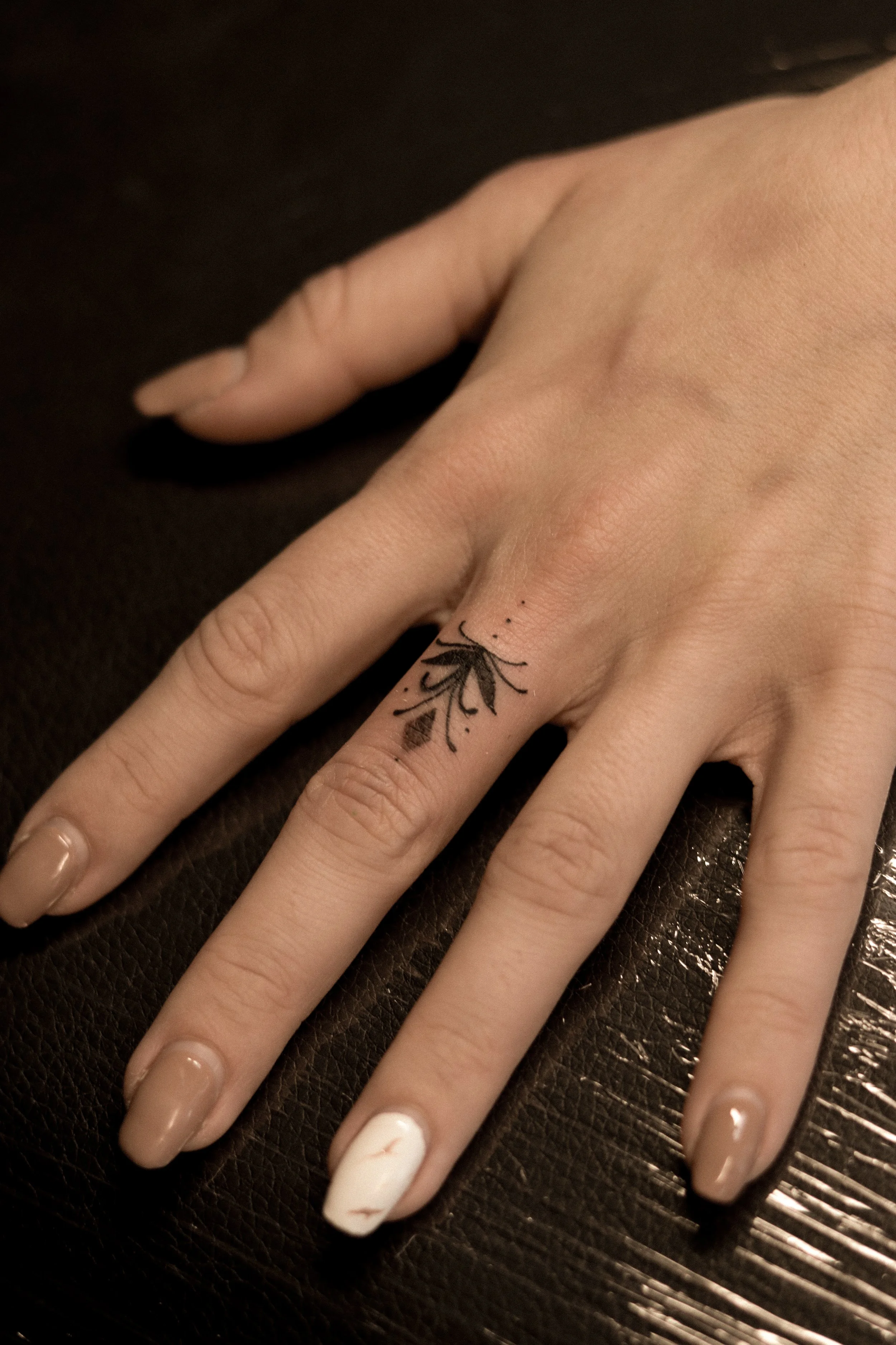 Hand met een ringvinger tattoo van een bloemen- of bladontwerp, op een donkere achtergrond.