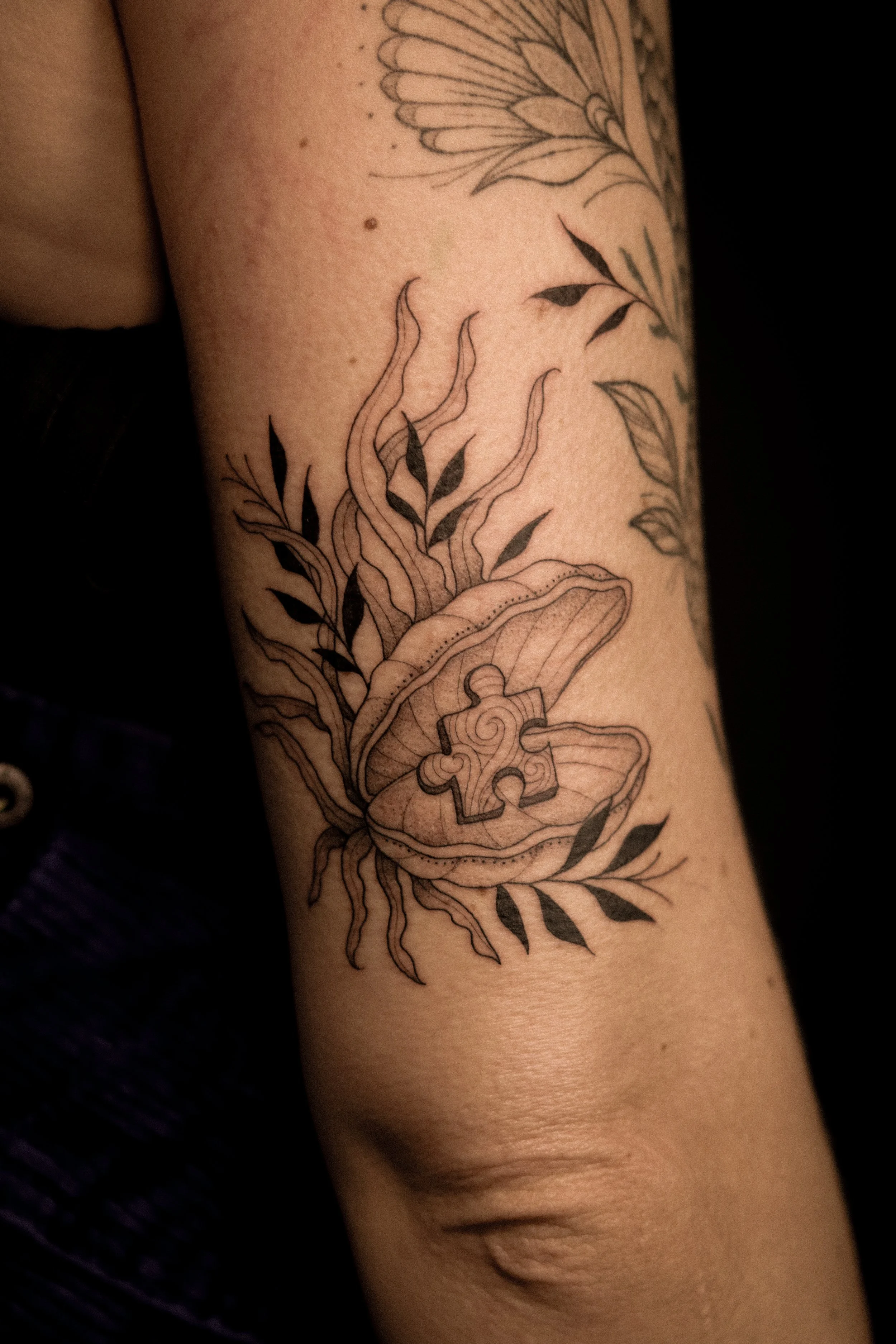 Tattoo van een paddestoel met een puzzelstukje op de hoed, omgeven door bladeren en planten.