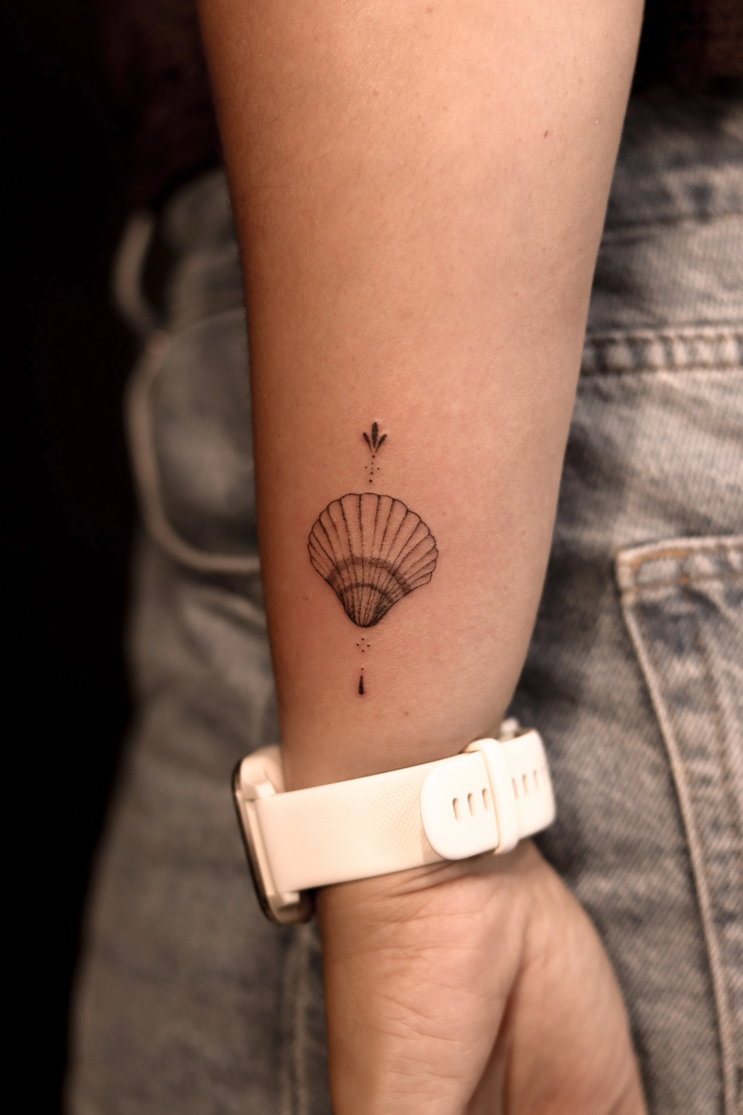 Tattoo van een schelp met druppel en abstracte symbolen op de onderarm.