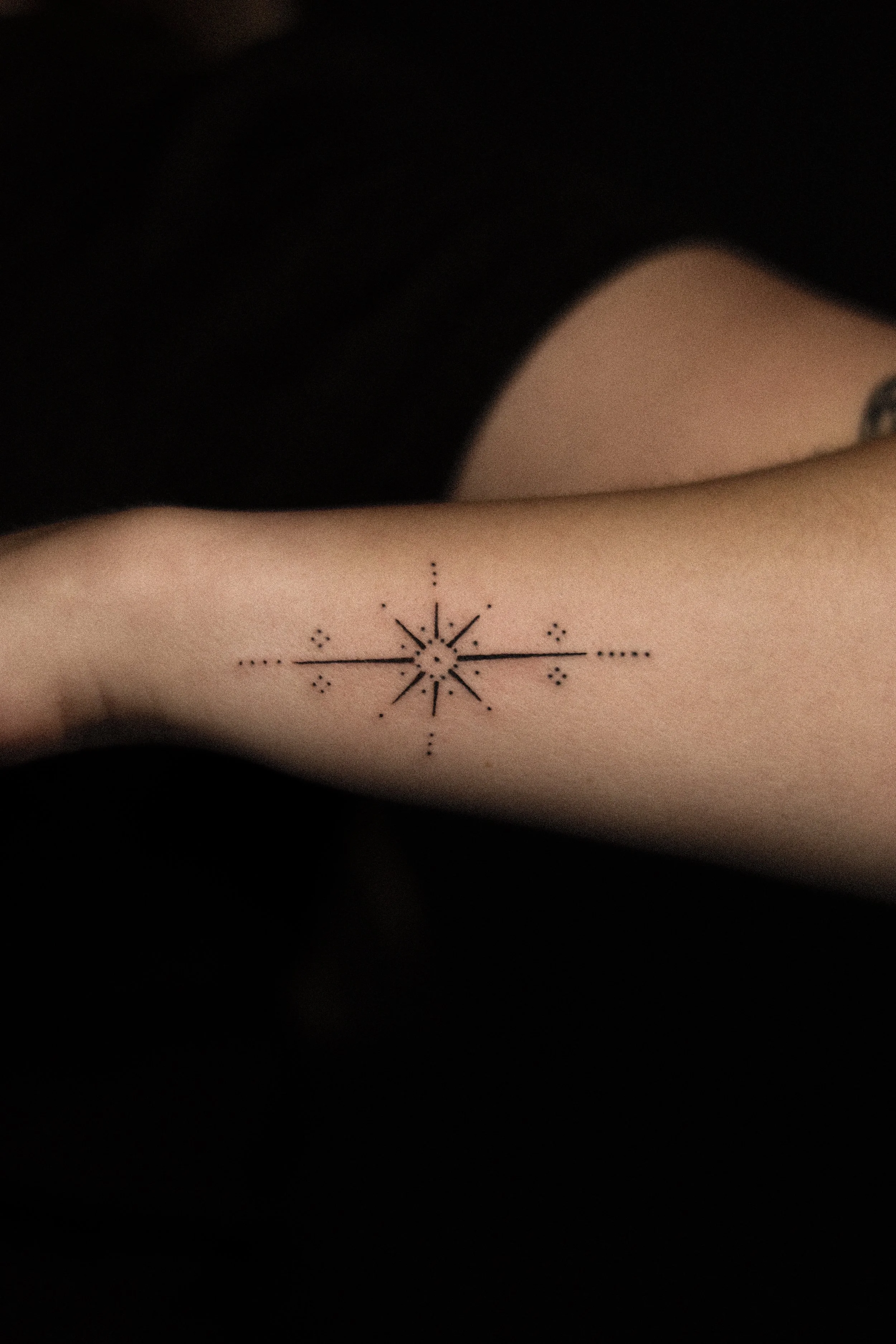 Tattoo van een geometrisch sterpatroon op een onderarm, met stralen en stippen.