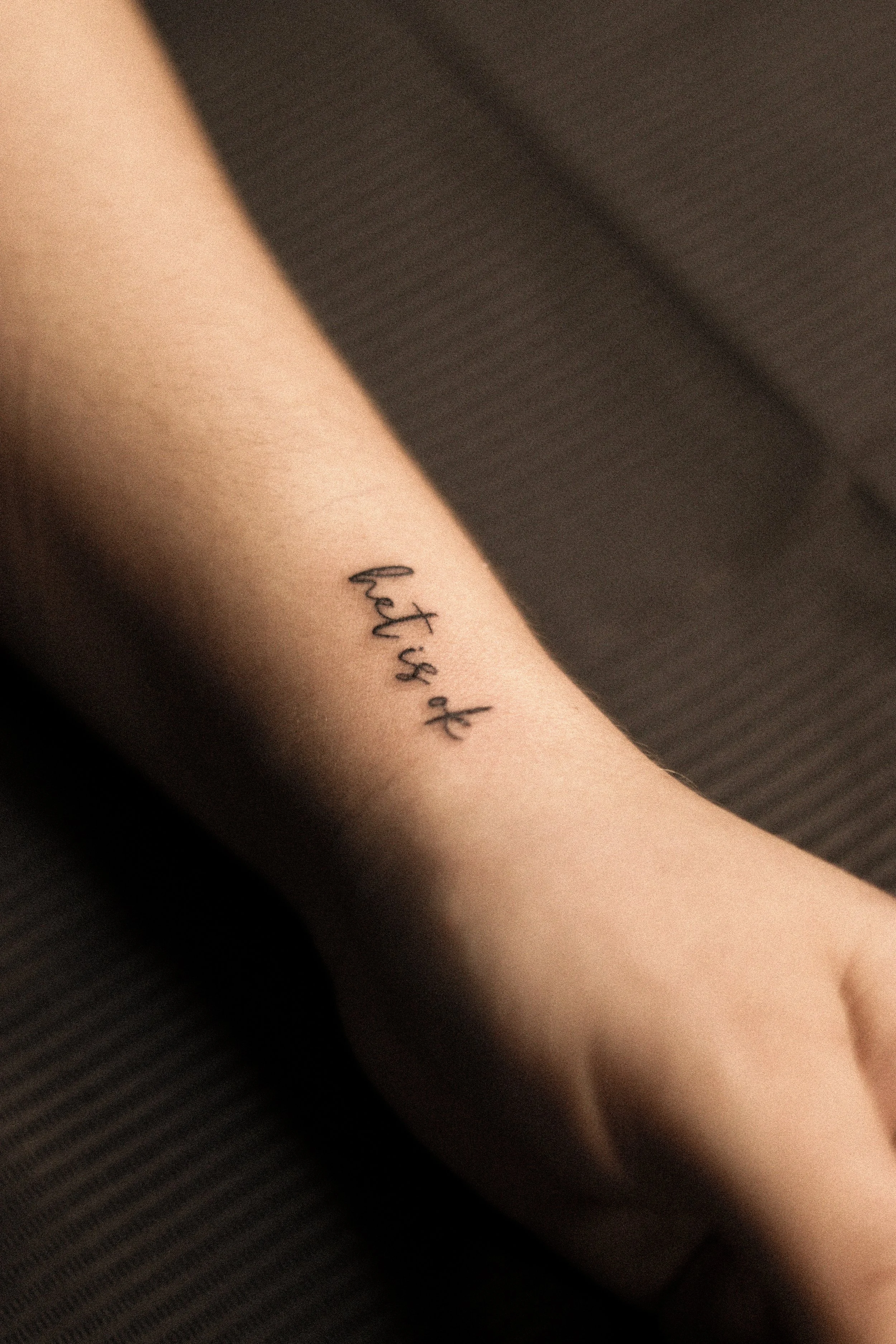 Tatoeage op arm met de tekst 'let's ok' in kleine, zwarte letters