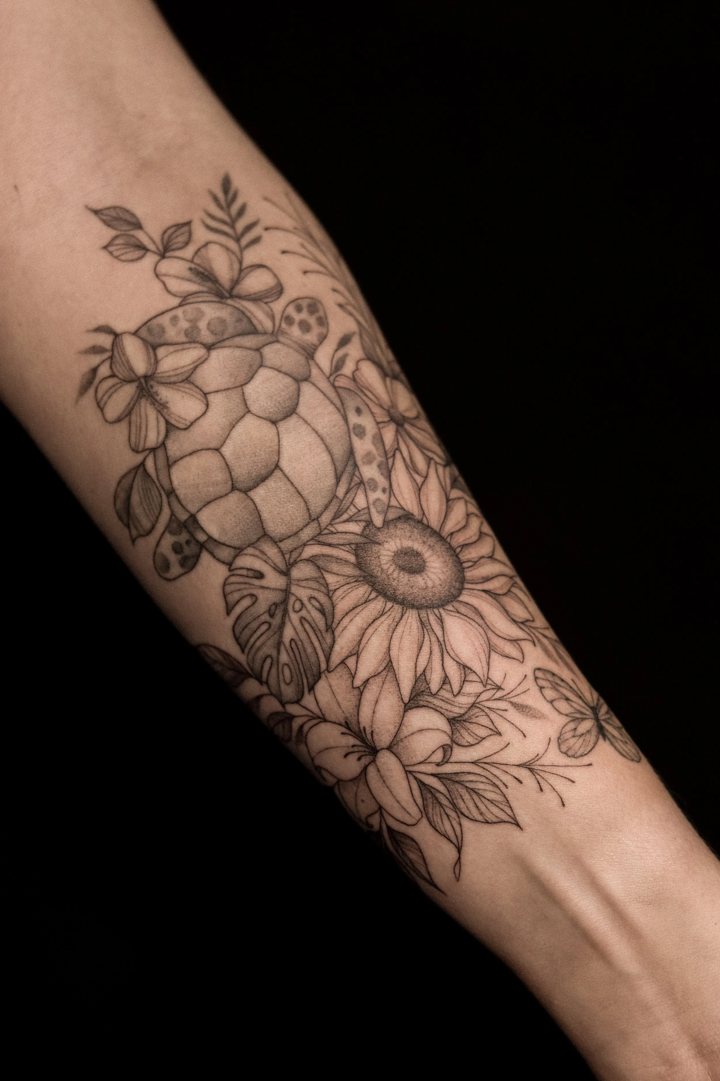 Lijntekening van een zeehond, bloemen, bladeren, een bij en een libel op een arm.