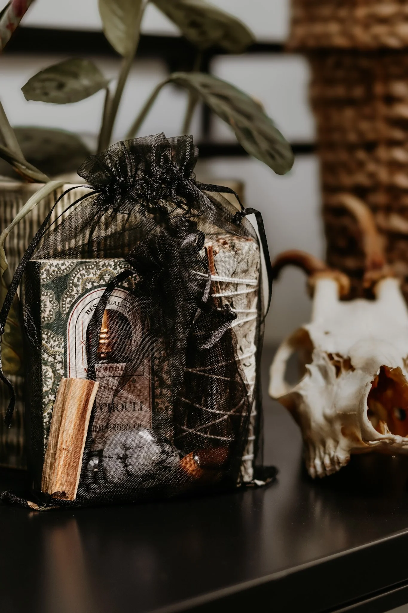 Een zwarte stoffen zak gevuld met diverse spullen, geplaatst op een zwarte plank met een giftige dierenschedel ernaast, en een plant op de achtergrond.