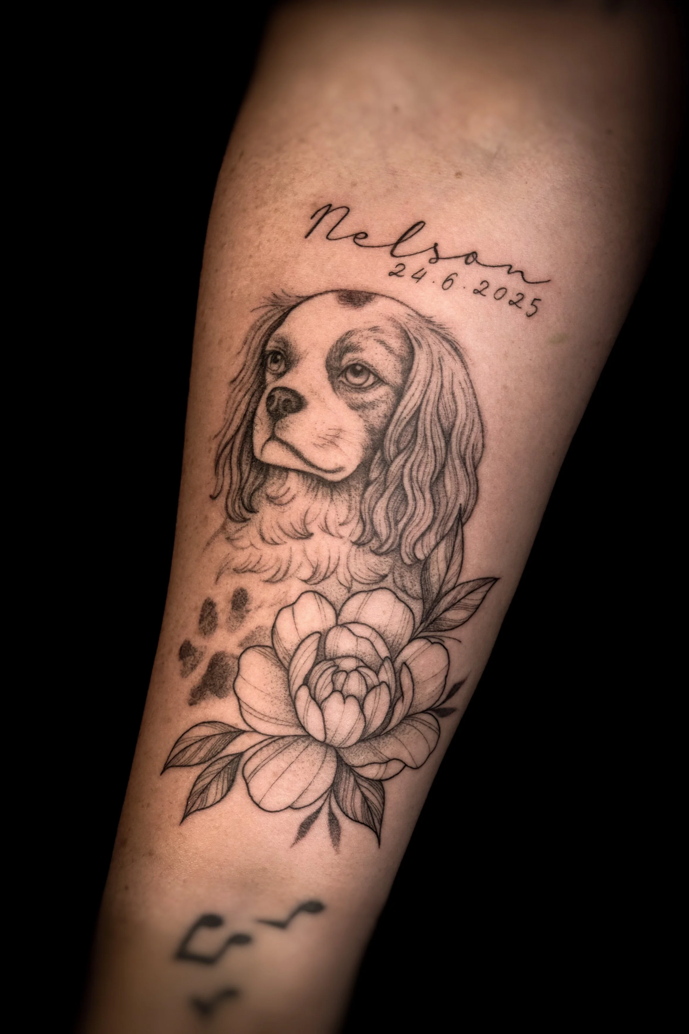 Tatoeage van een hondenhoofd, een bloem en tekst met een naam en datum.