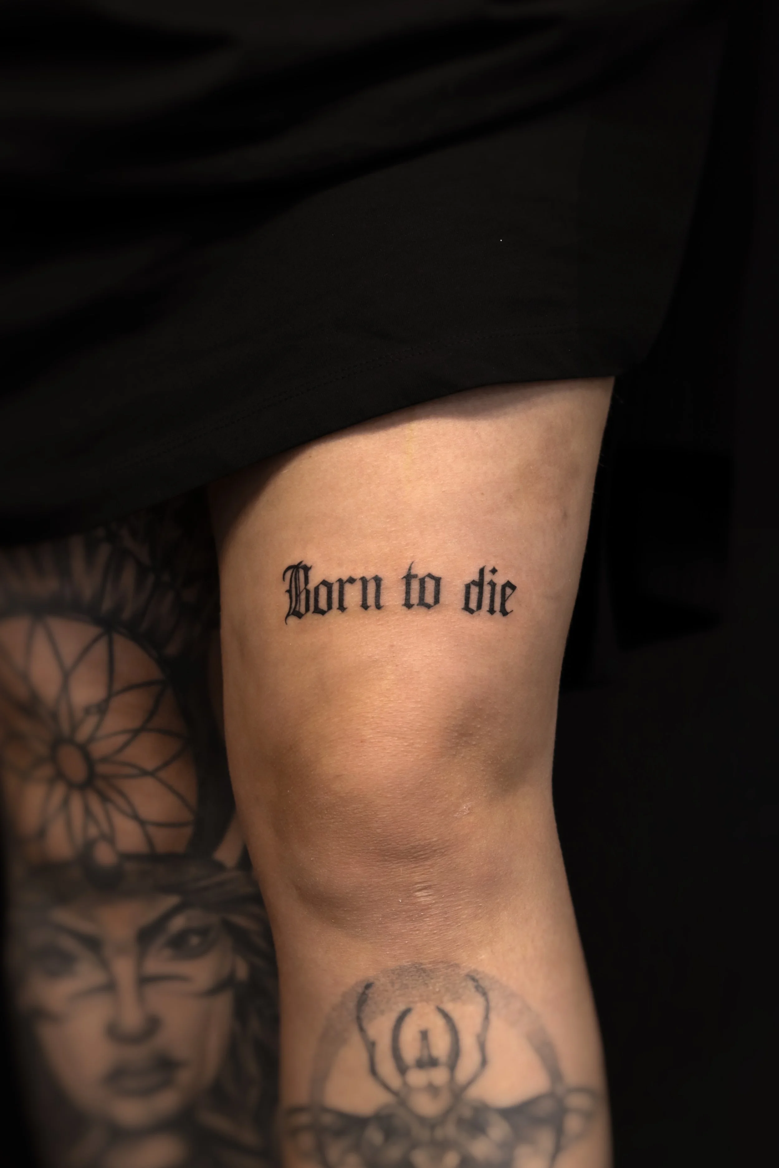 Tattoo op de bovenarm met de tekst 'Born to die' in zwarte gotische letters.