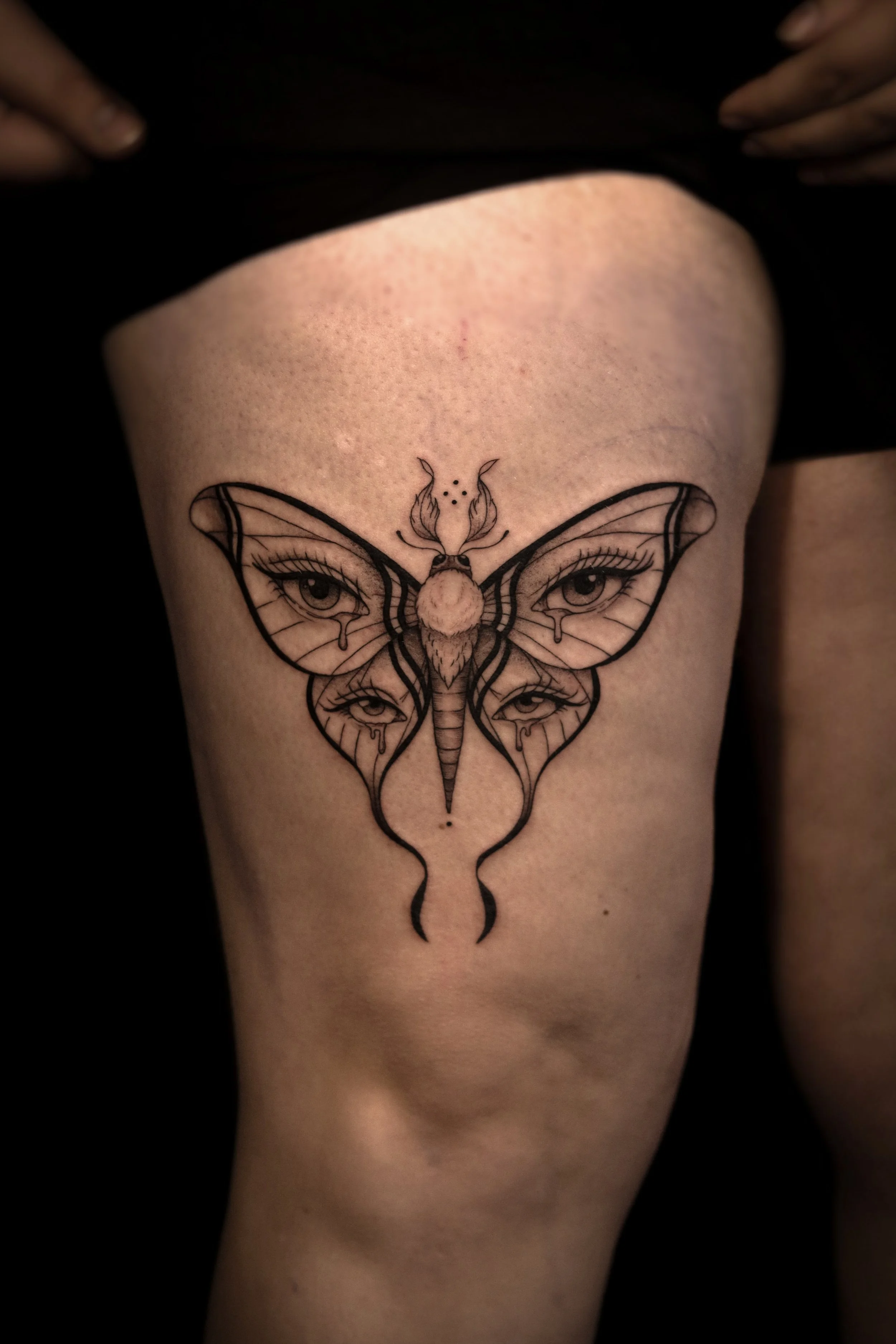 Tatoeage van een vlinder met gezichtselementen op de vleugels op een dij.