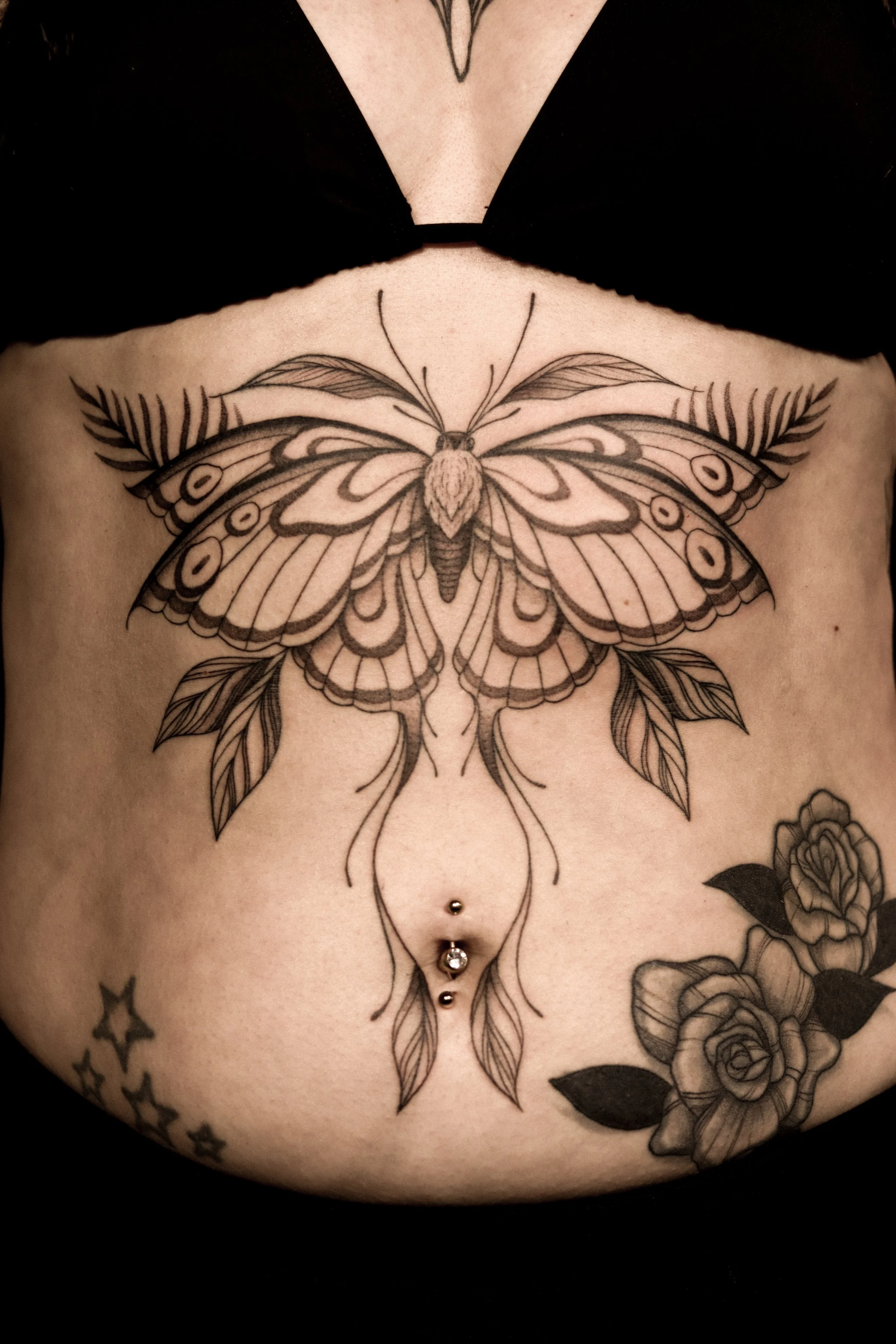 Tattoo van een grote vlinder met bloemen en bladeren op de onderbuik.