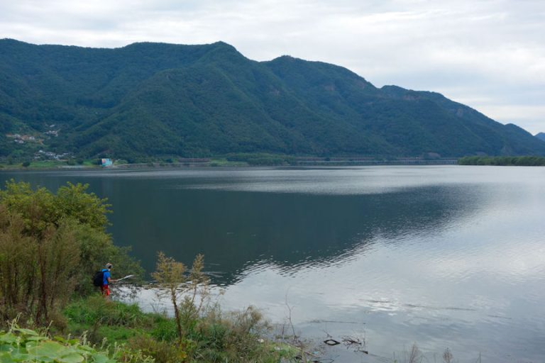 Person fishing by a lake with mountains in the background