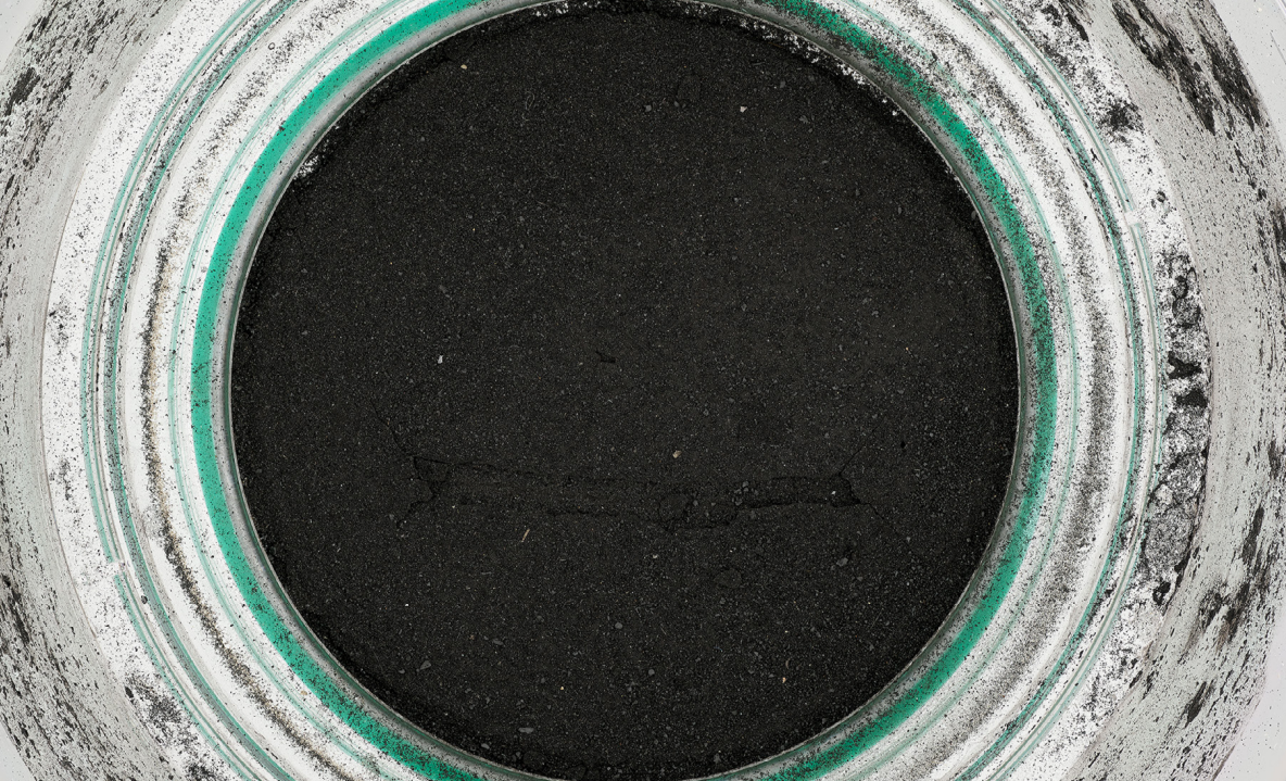 Close-up view of a large, round manhole opening with a cracked, dark interior and a greenish outer rim.