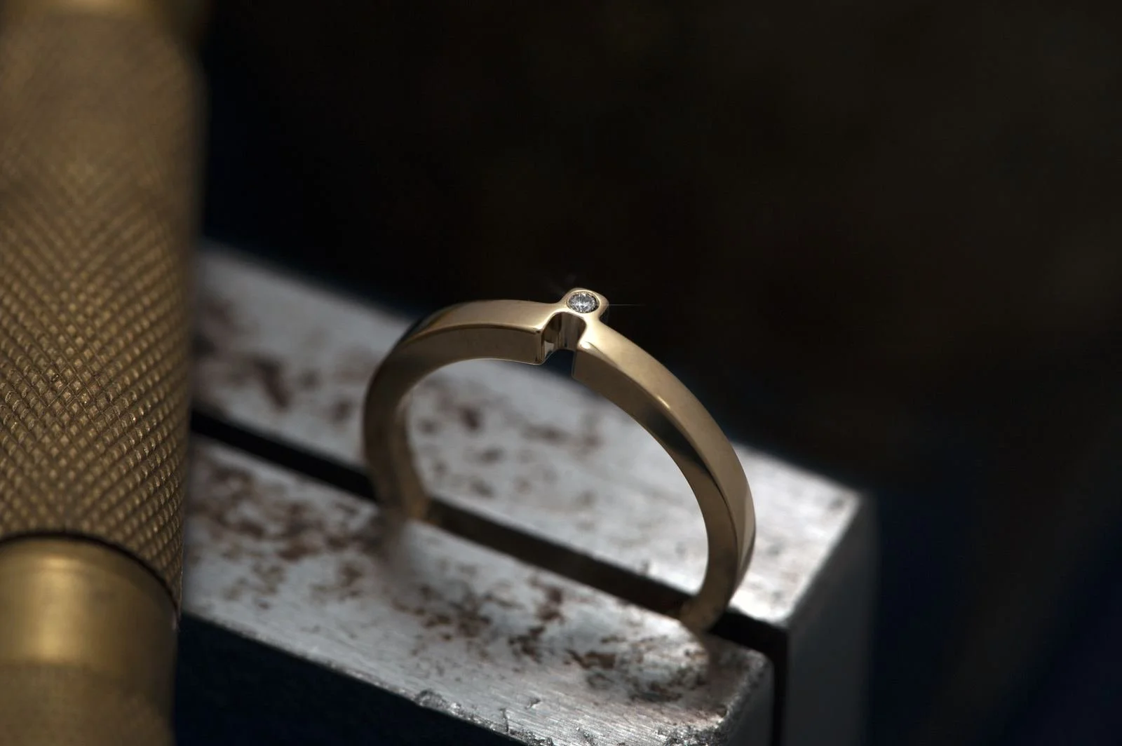 A gold ring with a small diamond set at the top, resting on the edge of a textured surface. Oyukio rings.