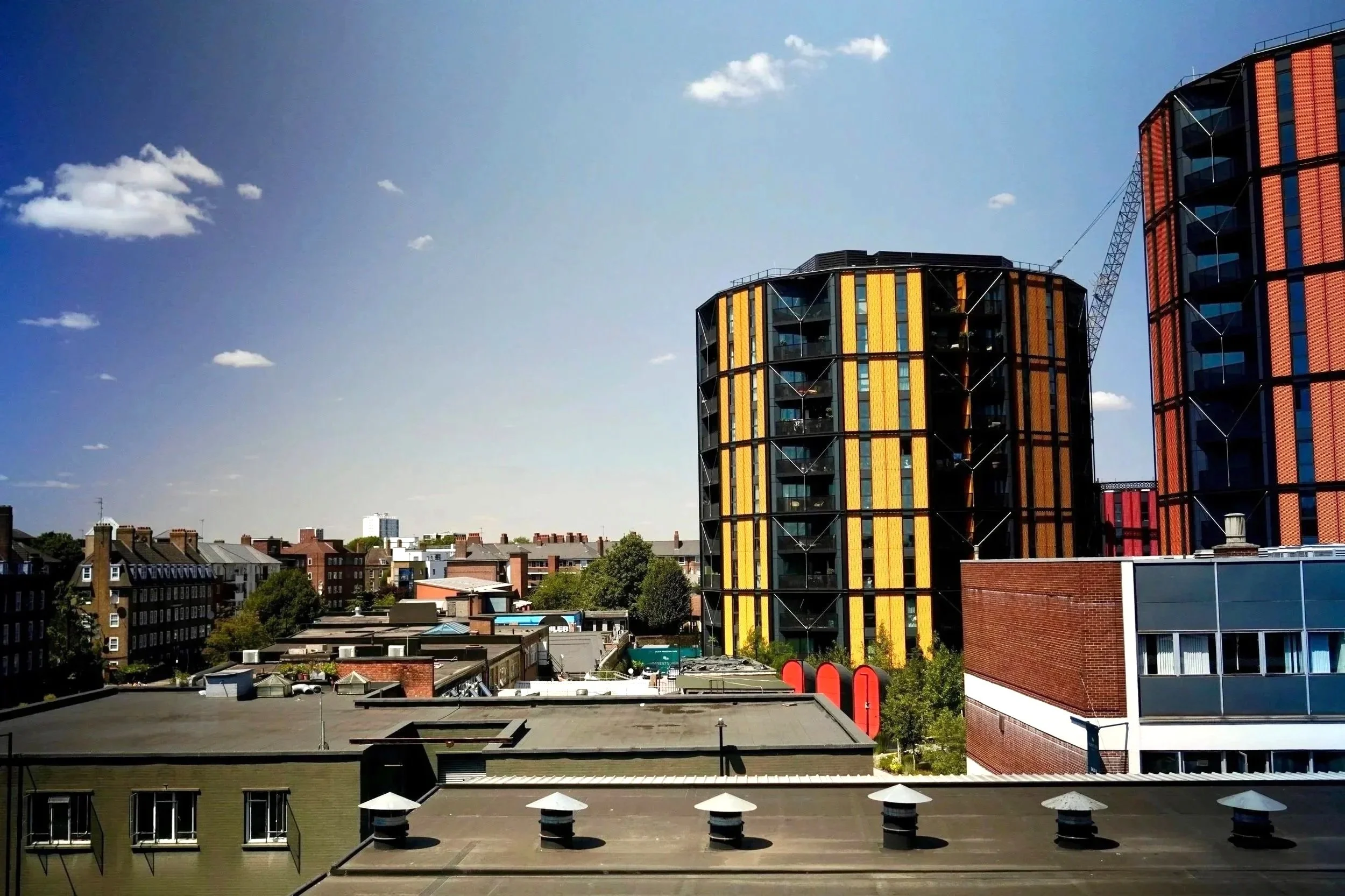 View of a cityscape with modern high-rise buildings and smaller residential structures under a bright blue sky with scattered clouds.