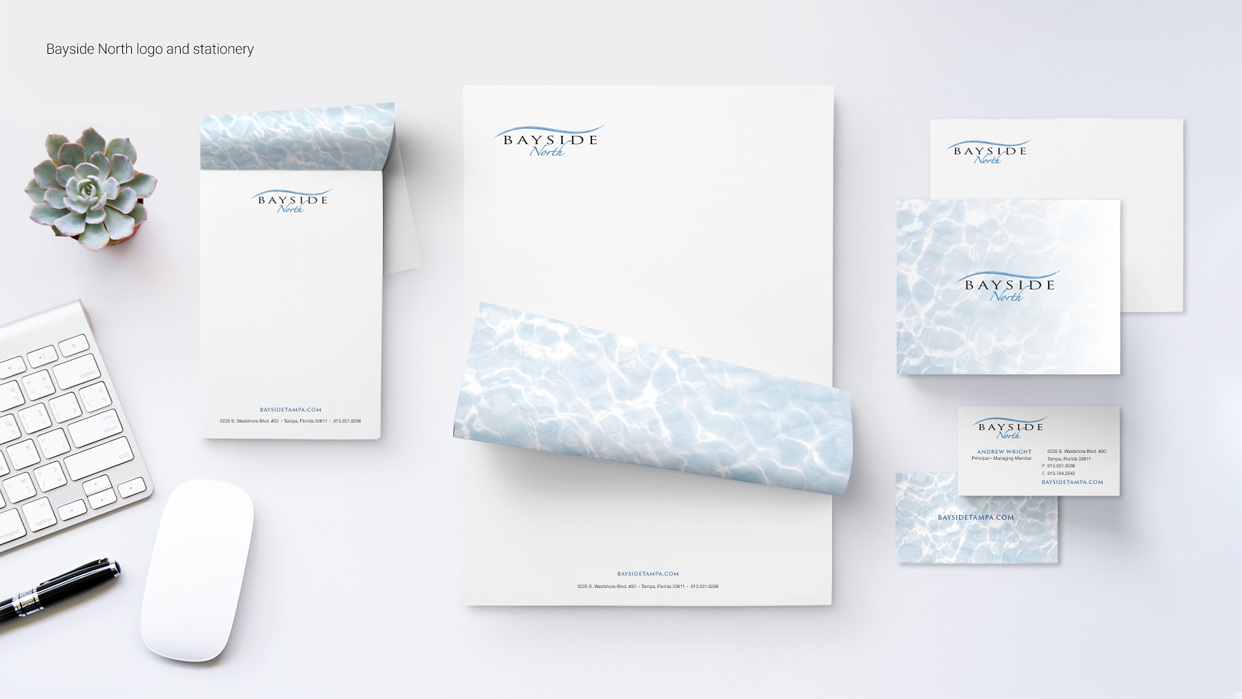 Stationery set with Bayside North logo, including letterhead, envelopes, and business cards with a blue water pattern, placed on a white desk with a succulent plant, keyboard, mouse, and pen.