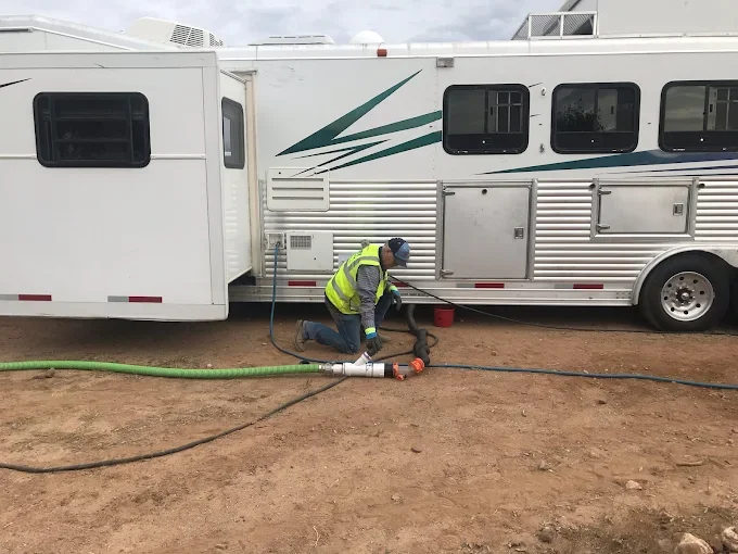 A man hooking up to a black water tank and a living quarters horse trailer.