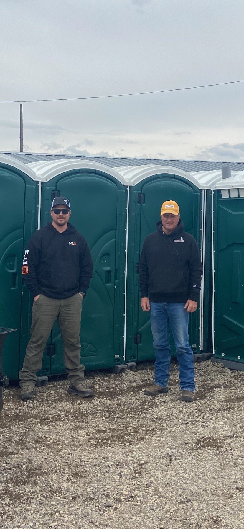 Two men standing in front of green porta potties