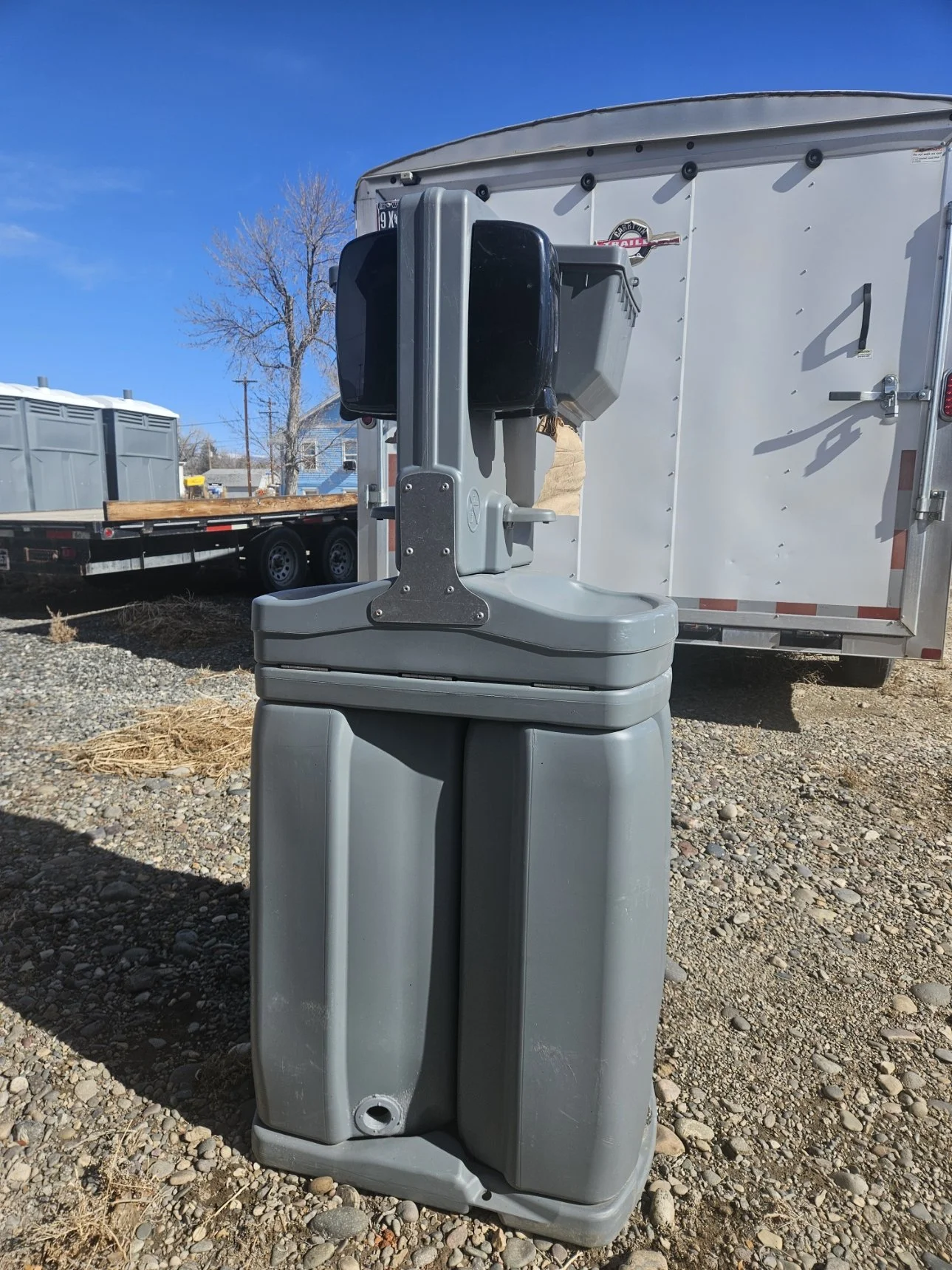 Portable handwashing station outdoors with a trailer and trees in the background.