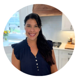Smiling woman with long dark hair wearing a navy sleeveless top in a kitchen.