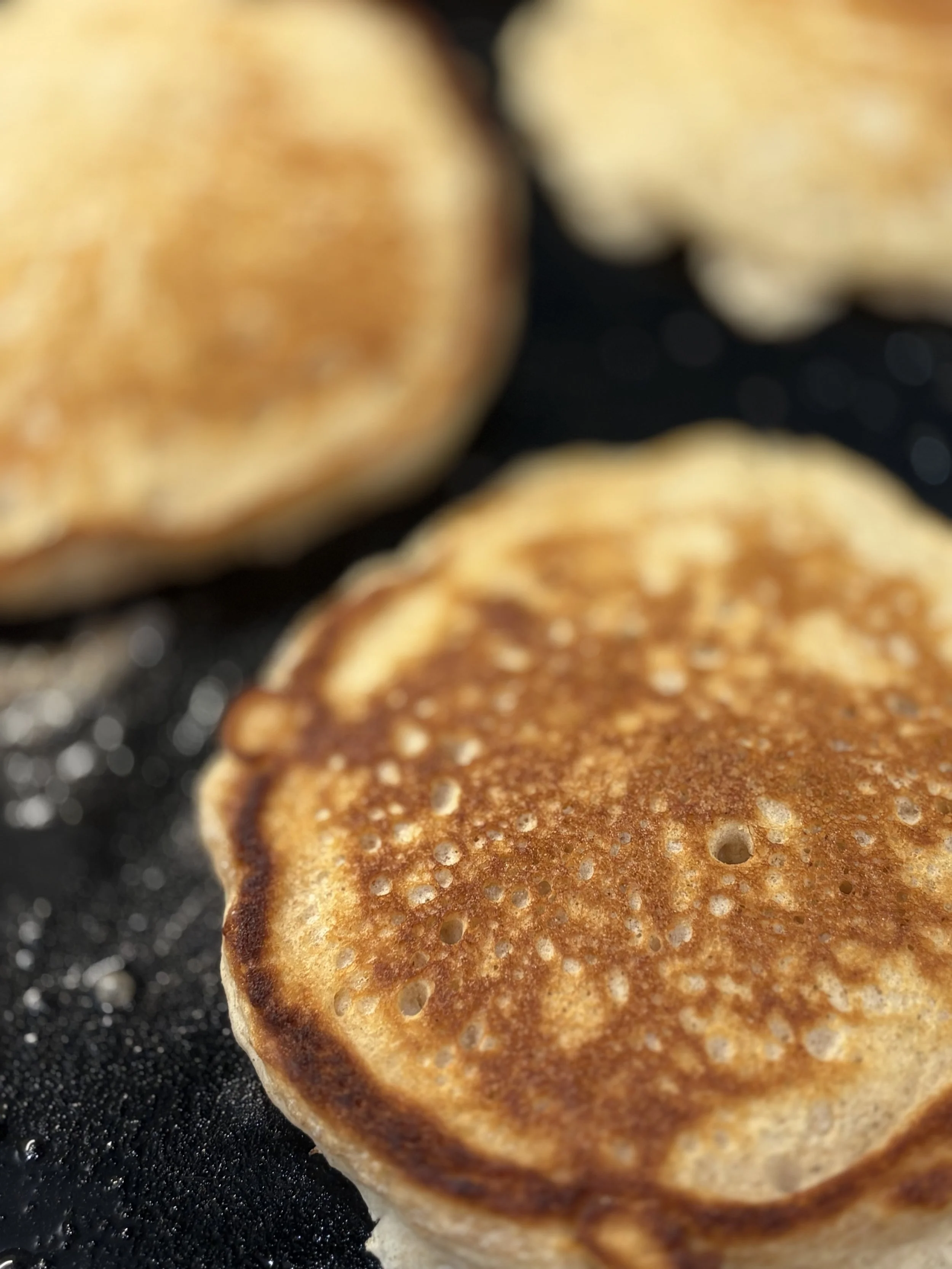 Close-up of golden-brown pancakes cooking on a black griddle.