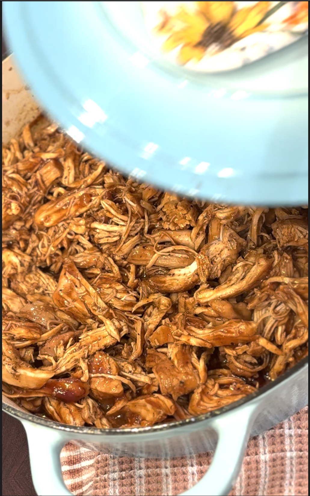 Shredded chicken cooked in barbecue sauce in a pot, viewed from above with part of a light blue lid visible.