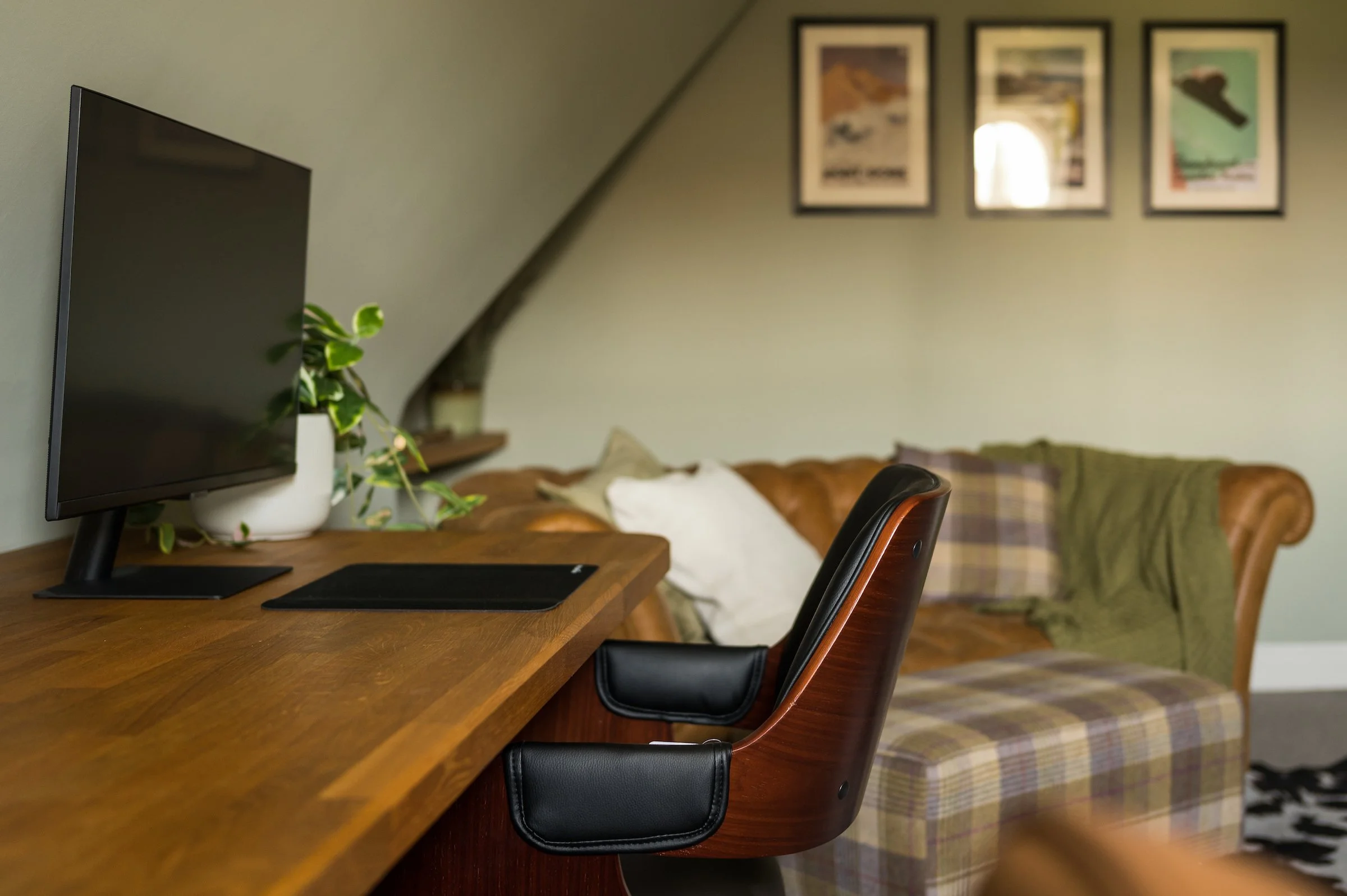 Living room with a beige couch, wooden coffee table, blue armchair with a pink pillow, window with curtains, flat-screen TV, potted plant, fireplace, framed pictures, and decorative circles on the wall.