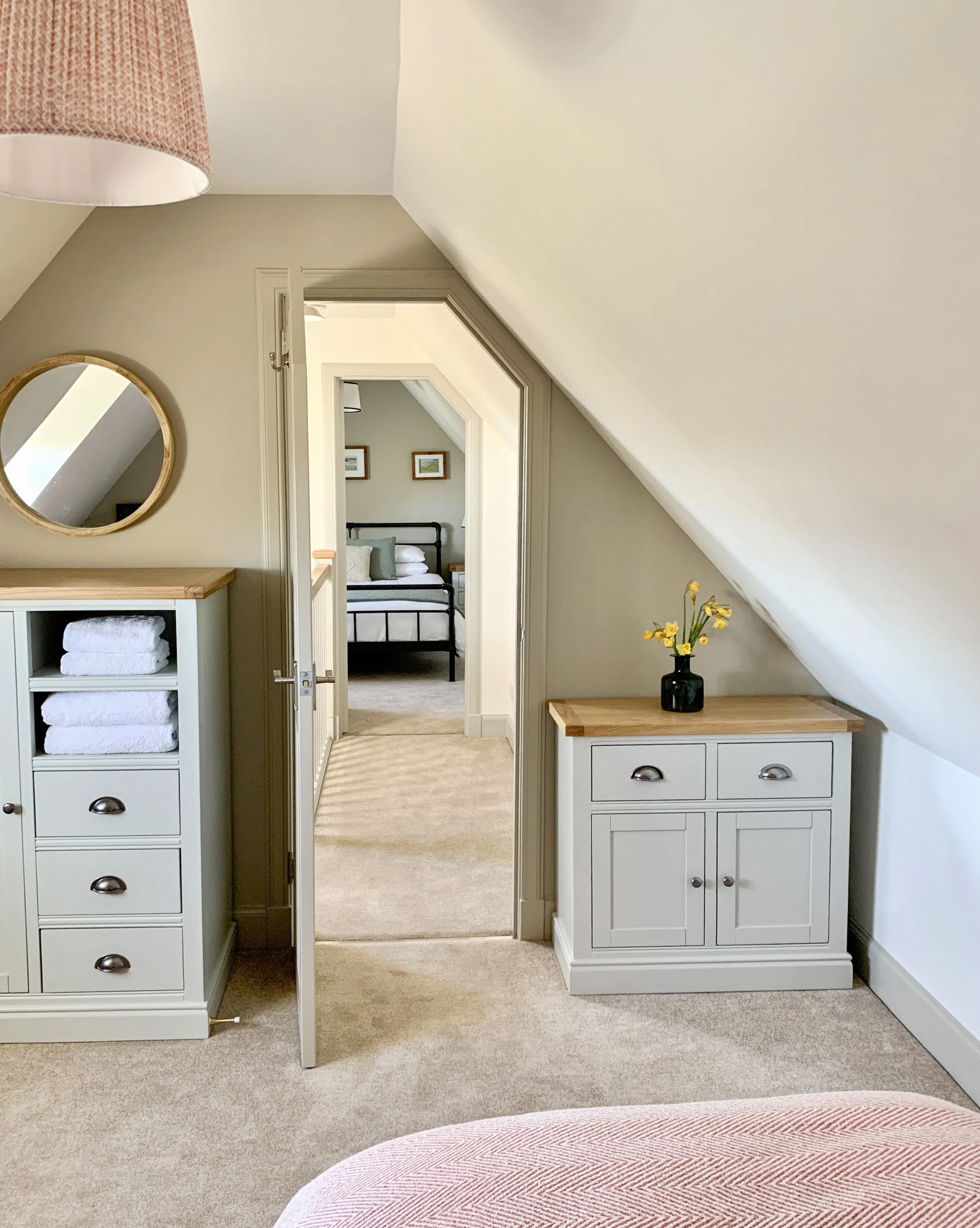 Living room window seat with cushions, wooden dining table with chairs, a vase of flowers, and view of trees and grass outside