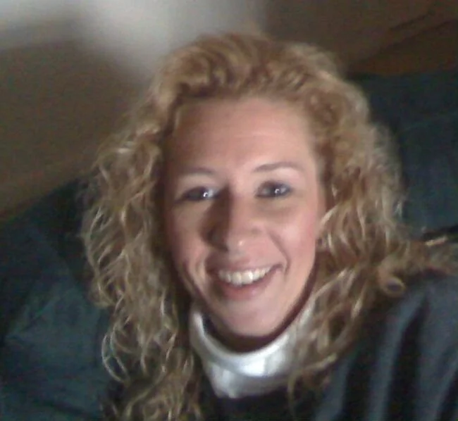 A woman with curly blonde hair smiling at the camera.