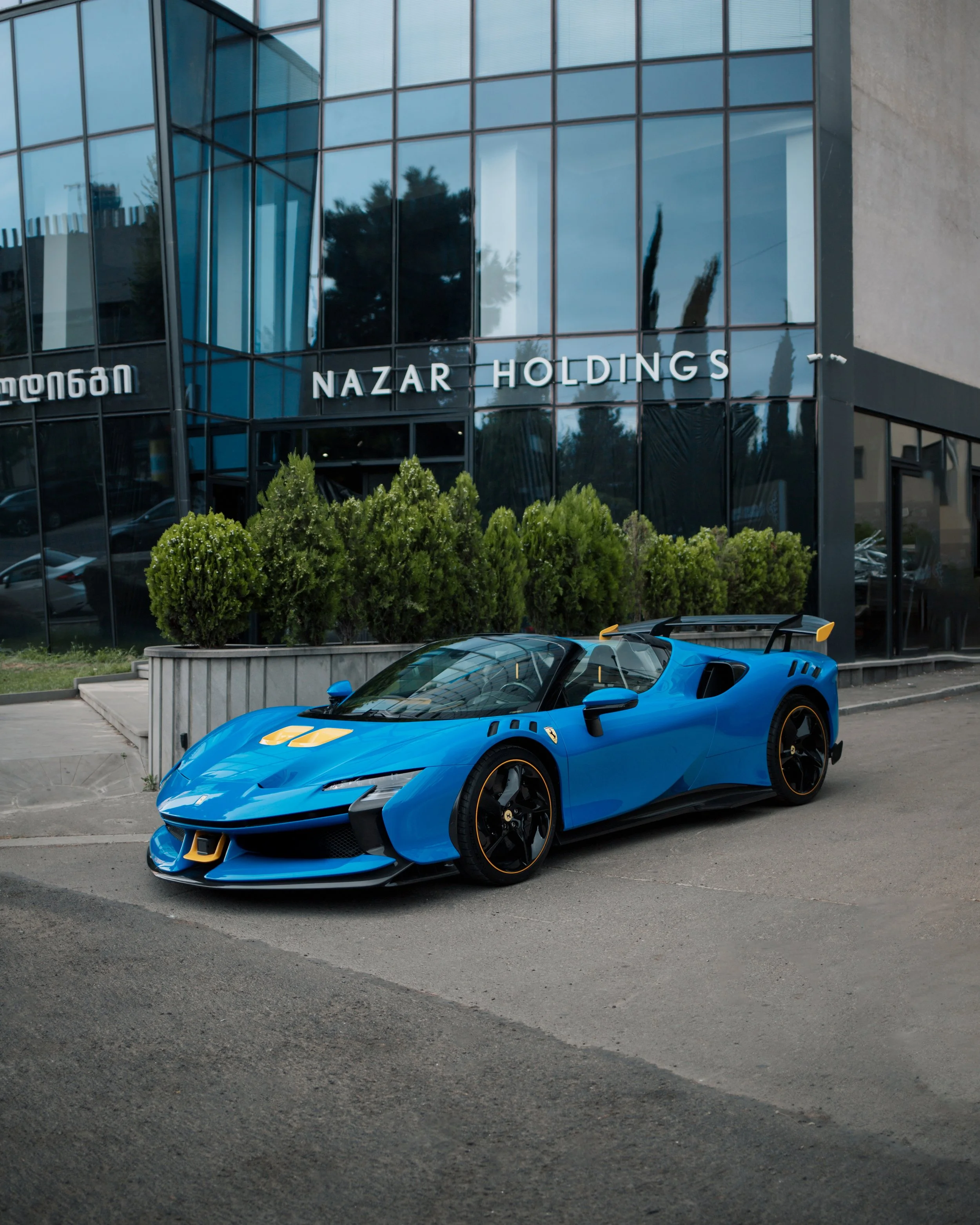 Blue sports car parked in front of a modern building with glass windows labeled 'Nazar Holdings'.