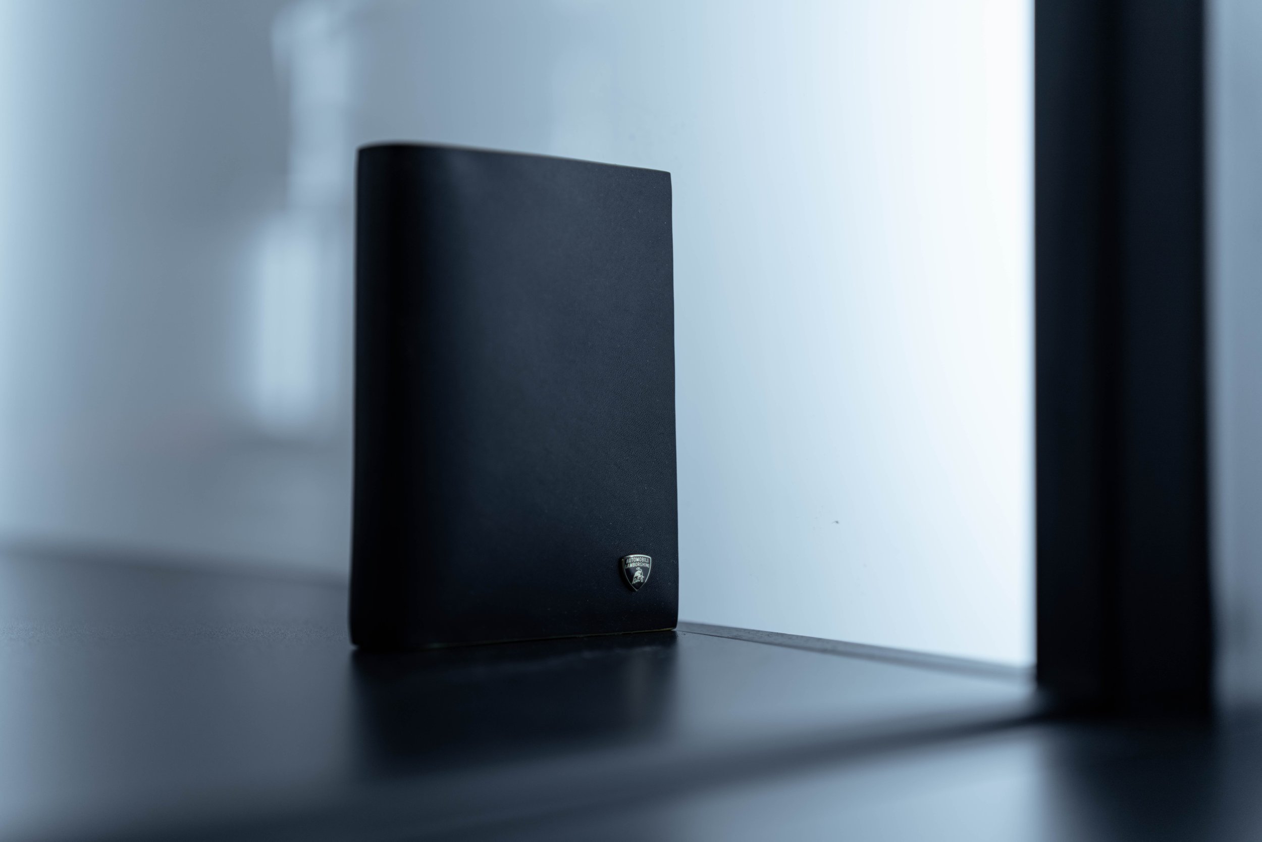Black speaker with Lamborghini emblem on a black surface, against a white wall and window.